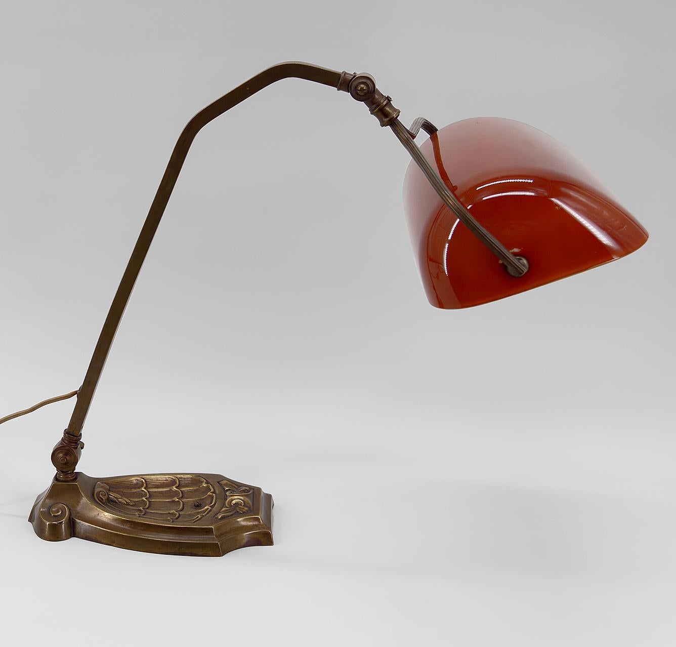 Superb banker's lamp / Emeralite with red / orange opaline glass shade and brass structure composed of a base and an articulated arm.

Art Nouveau, France, around 1900.

In very good condition, new opaline, electricity