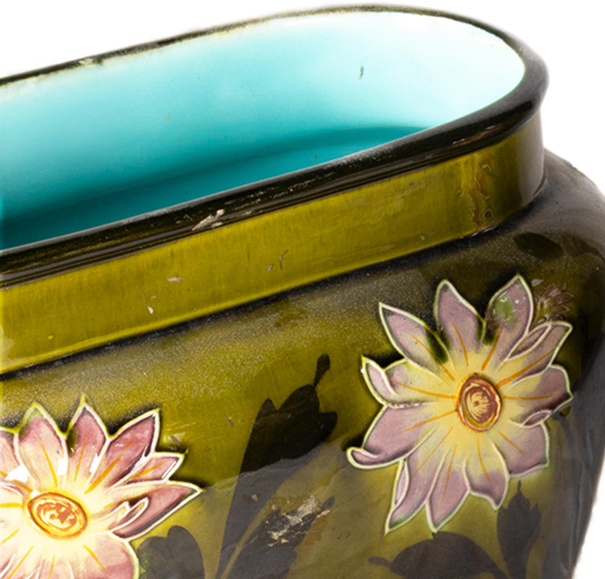 Un vase cachepot Art Nouveau faïence des années 1900 en France, en céramique vert olive avec des reliefs floraux en Barbotine. 
Les intérieurs sont finis dans un glaçage bleuâtre saisissant qui contraste élégamment avec les motifs floraux