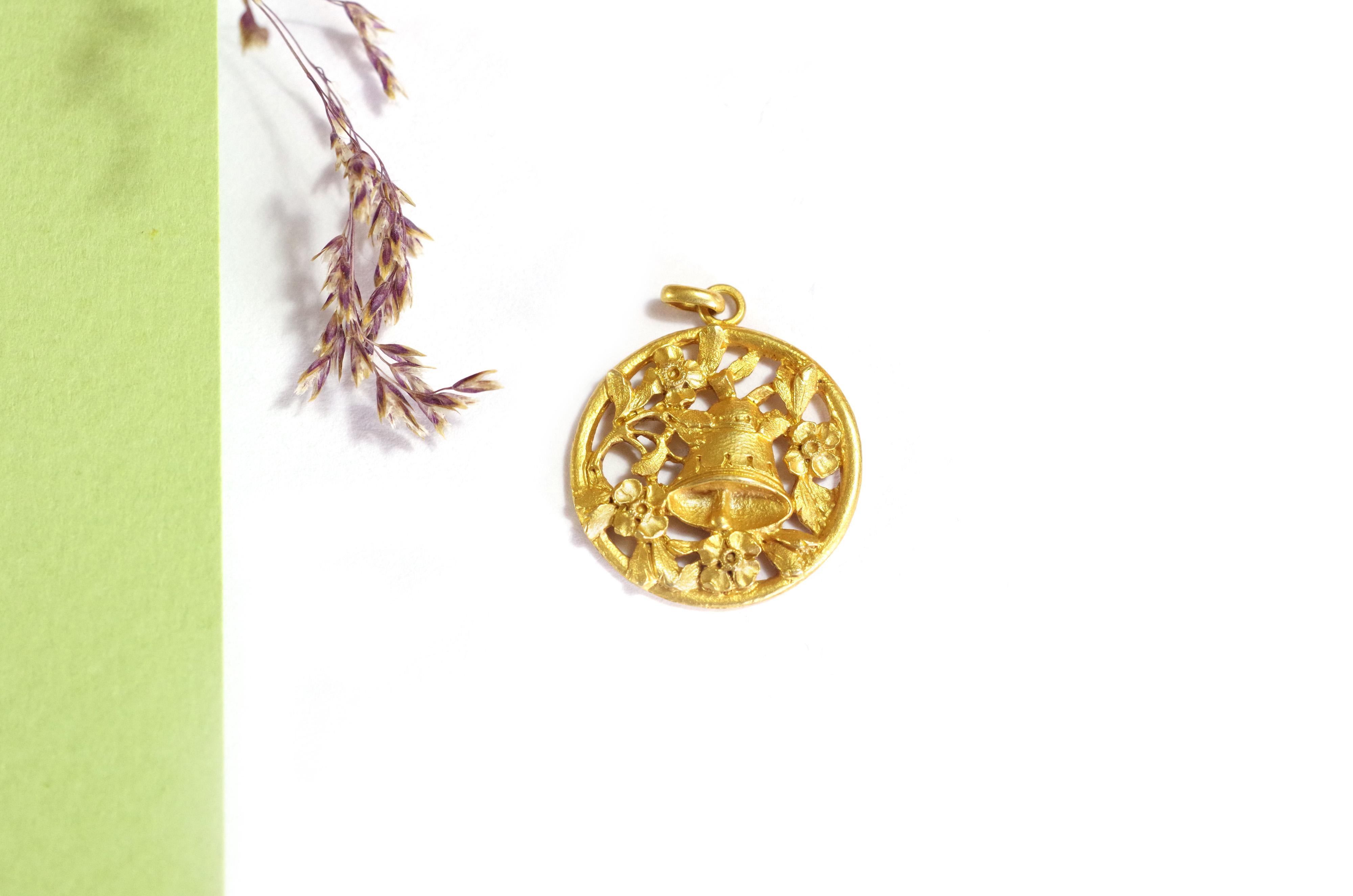 Art Nouveau bell gold medal in 18 karat yellow gold. In the center of the medal is a bell, surrounded by flowering branches. The jewel is openwork and matte gold. The bell probably represents the Angelus, a prayer traditionally announced three times