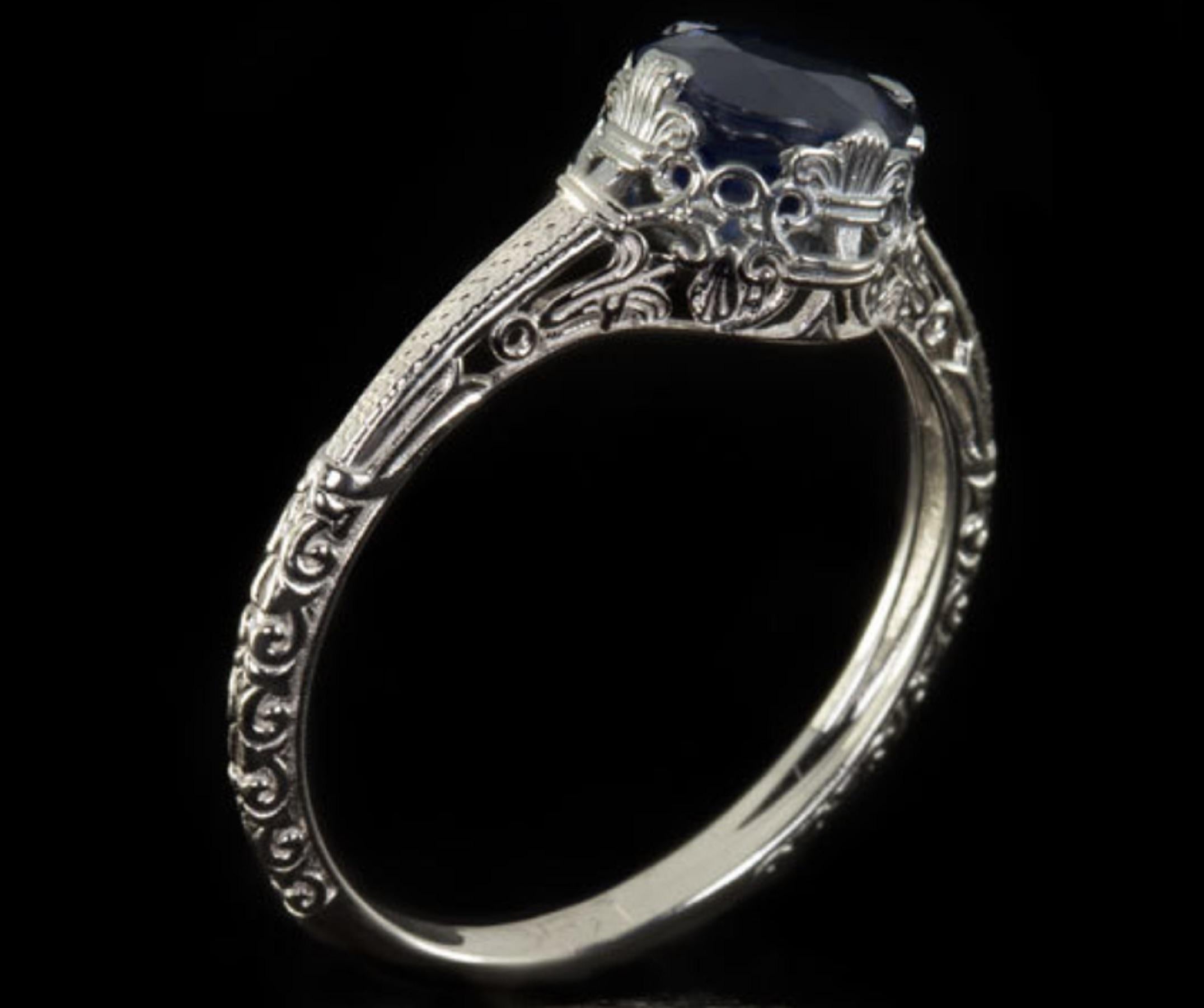 sapphire ring reminiscent of the 1920s Art Nouveau era. 

This beautiful ring features a single round cut natural sapphire (approximately 1ct) firmly prong set in the solid 14K White Gold band. This lovely sapphire measures 6mm wide and the ring is