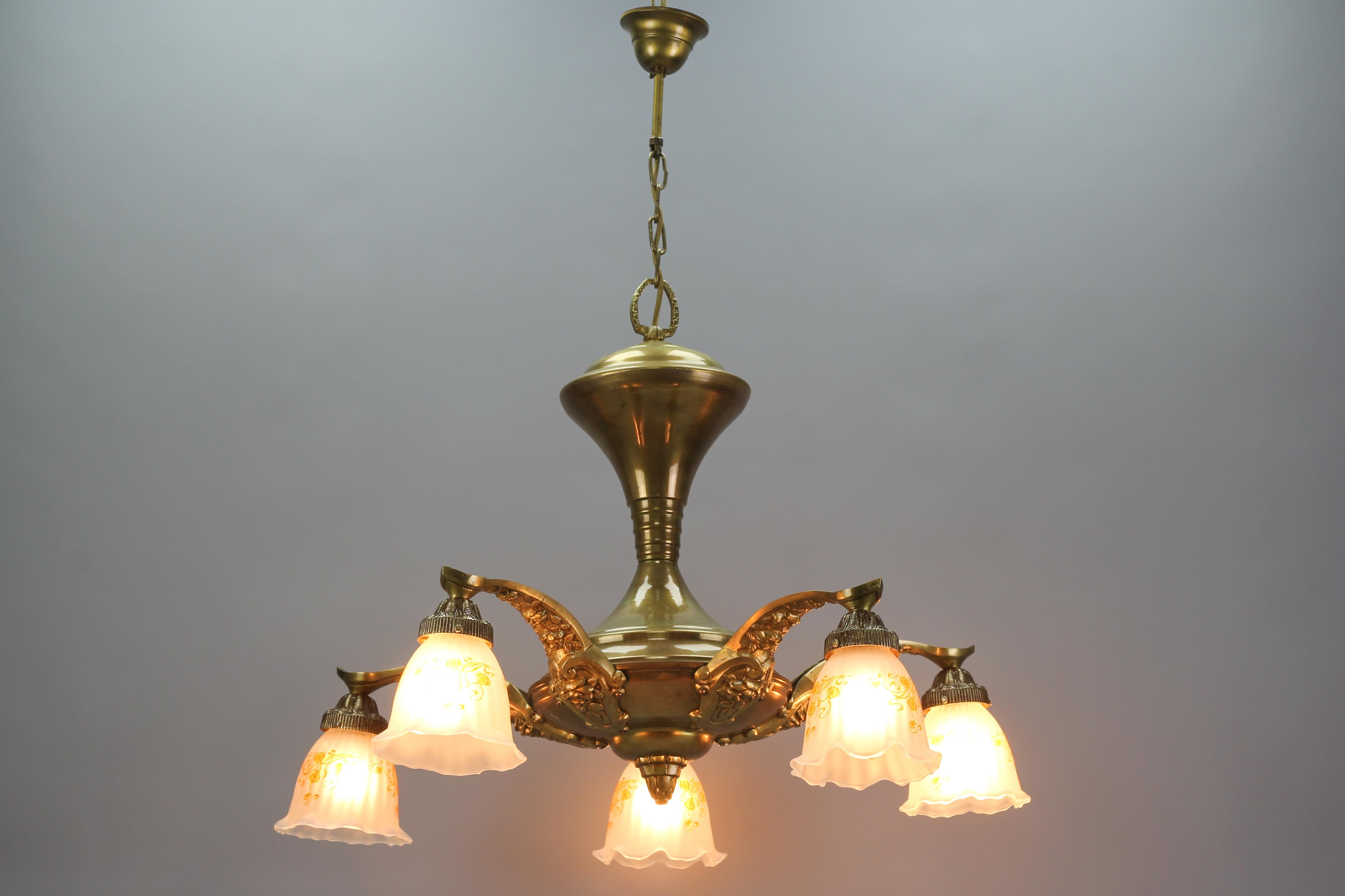 This beautiful French Art Nouveau chandelier features a brass central body and five arms, made of bronze and richly decorated with roses and rose leaves. Each arm has a white frosted glass shade with floral decoration in dark orange, and a socket