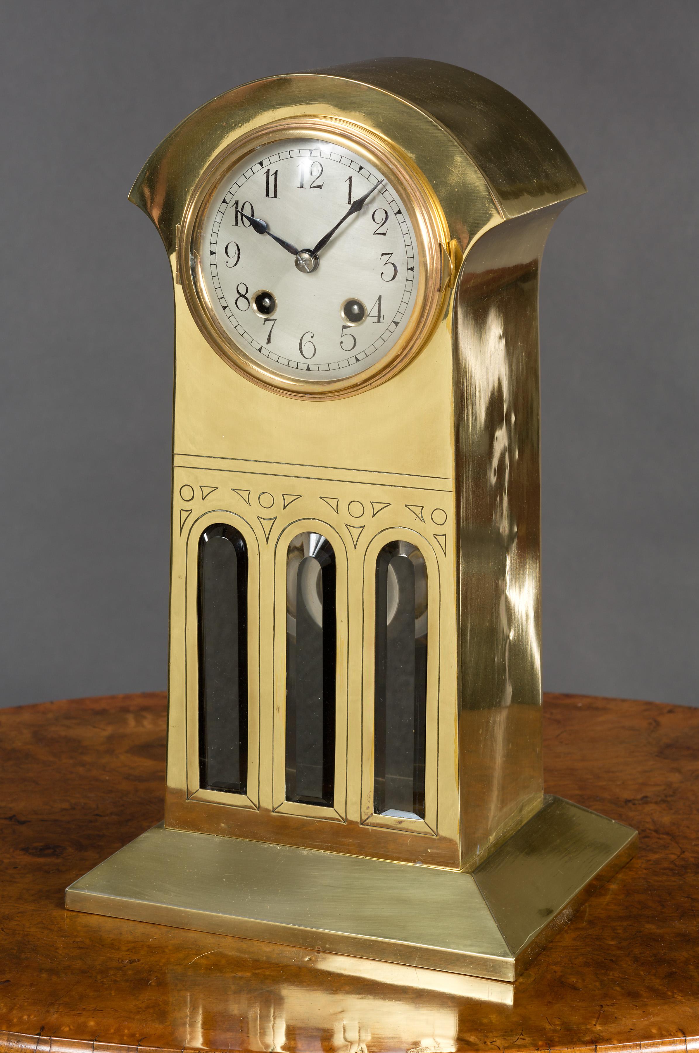 Art Nouveau brass cased mantel clock. The case standing on a sloping plinth with three glass panels to the front with engraved decoration.

Brass bezel opening to a silvered dial with Arabic numerals and original hands.

Silk lined sound fret to