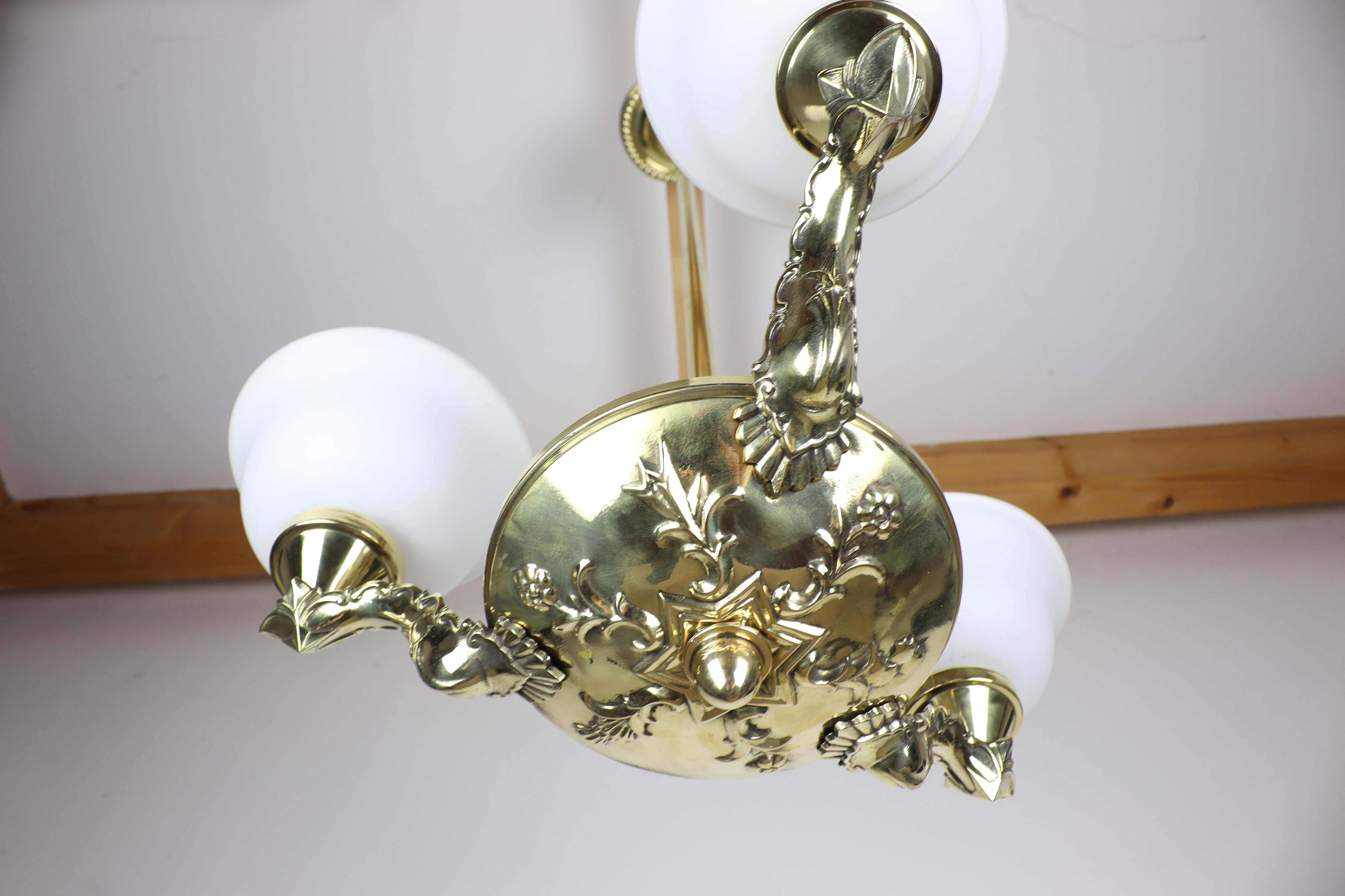 This luxurious-looking chandelier dates back to the Art Nouveau period. You will be fascinated by the beautifully elaborate embossed base of its three-shoulder design together with the glass shades in white adds elegance to the chandelier. This is a