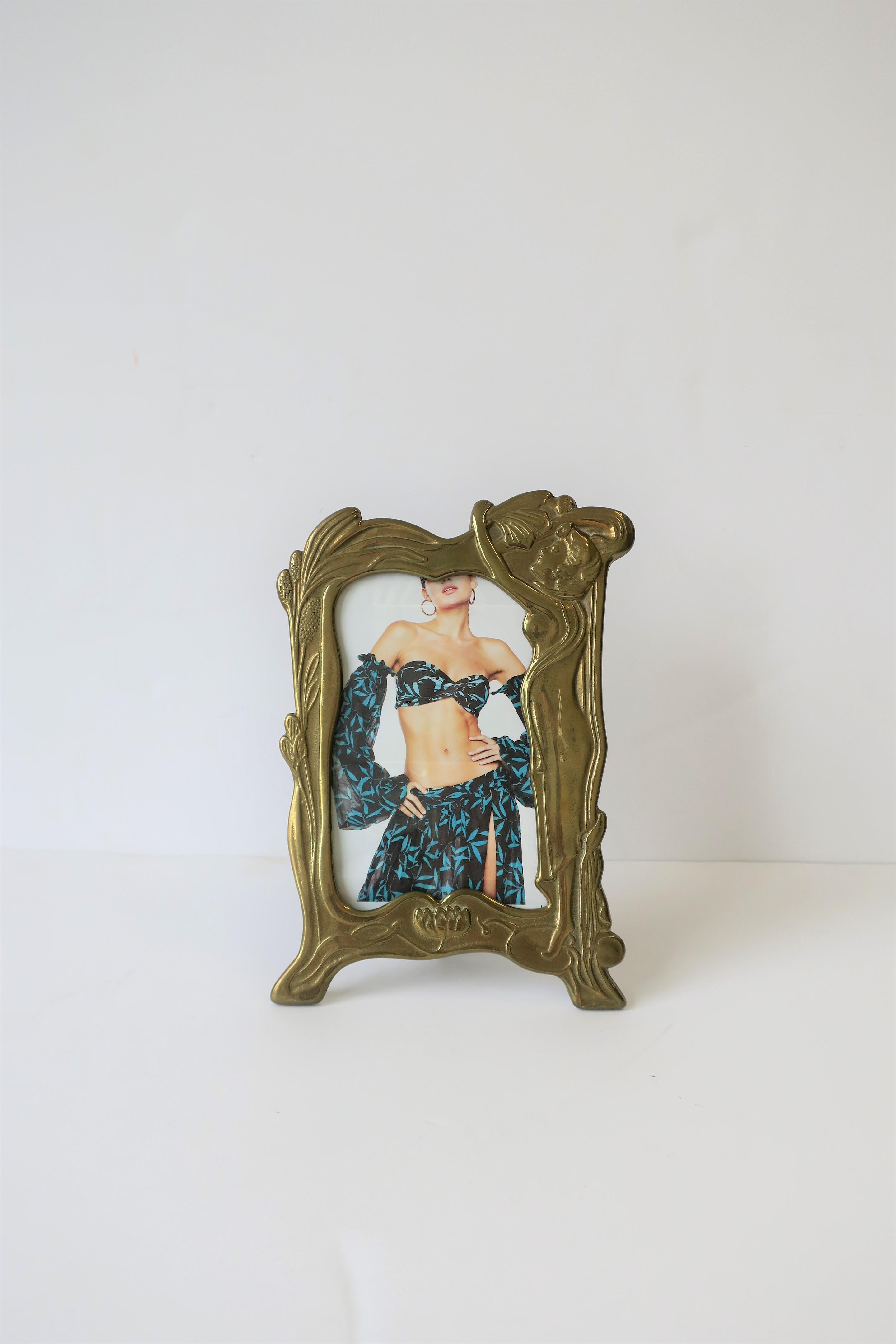 A beautiful Art Nouveau style brass picture frame, circa 20th century. Brass frame has beautiful female nude figure with lotus flower and leaf design around. Frame is solid brass with beautiful kickstand back. Overall frame dimensions: 6