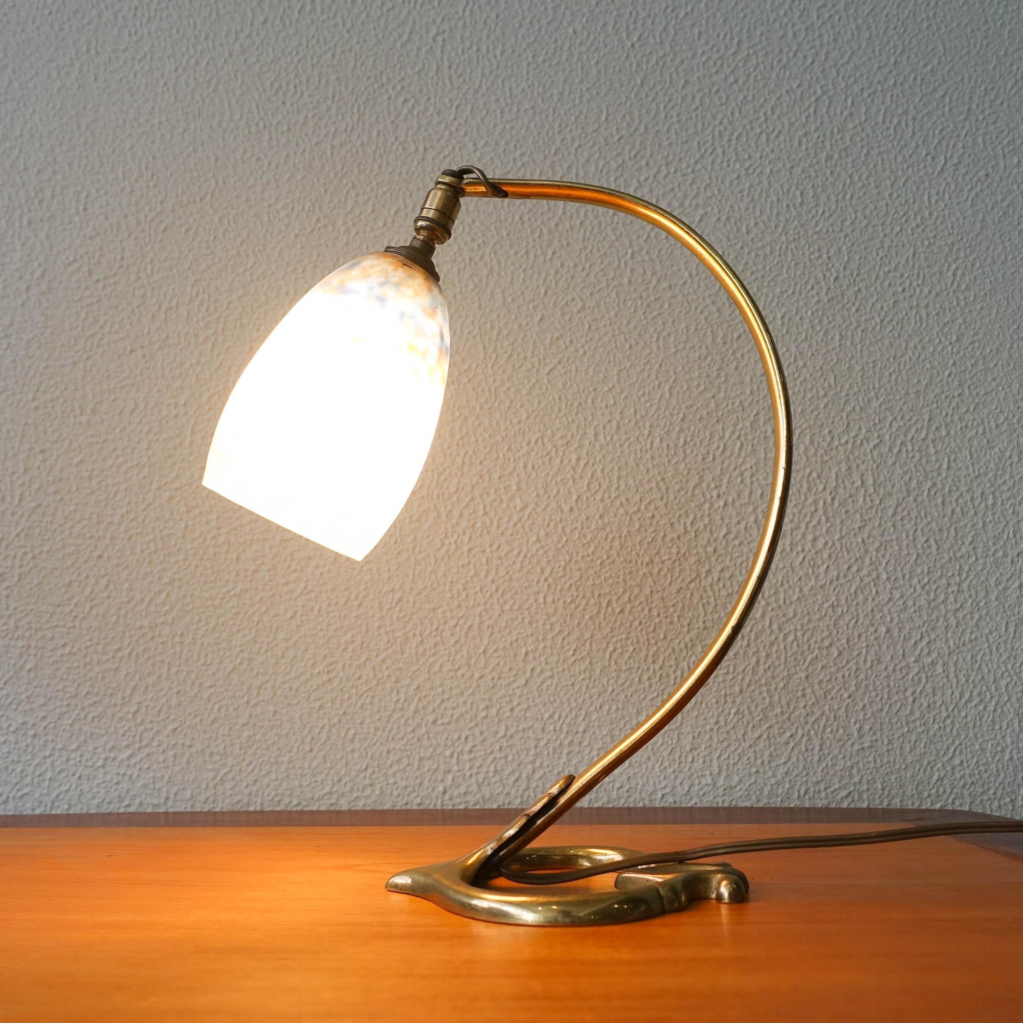 Cette lampe de table Art nouveau a été conçue et produite par Daum Nancy, en France, dans les années 1920. Elle possède un abat-jour en verre soufflé qui est suspendu dans un luminaire en bronze massif au design organique et incurvé, très