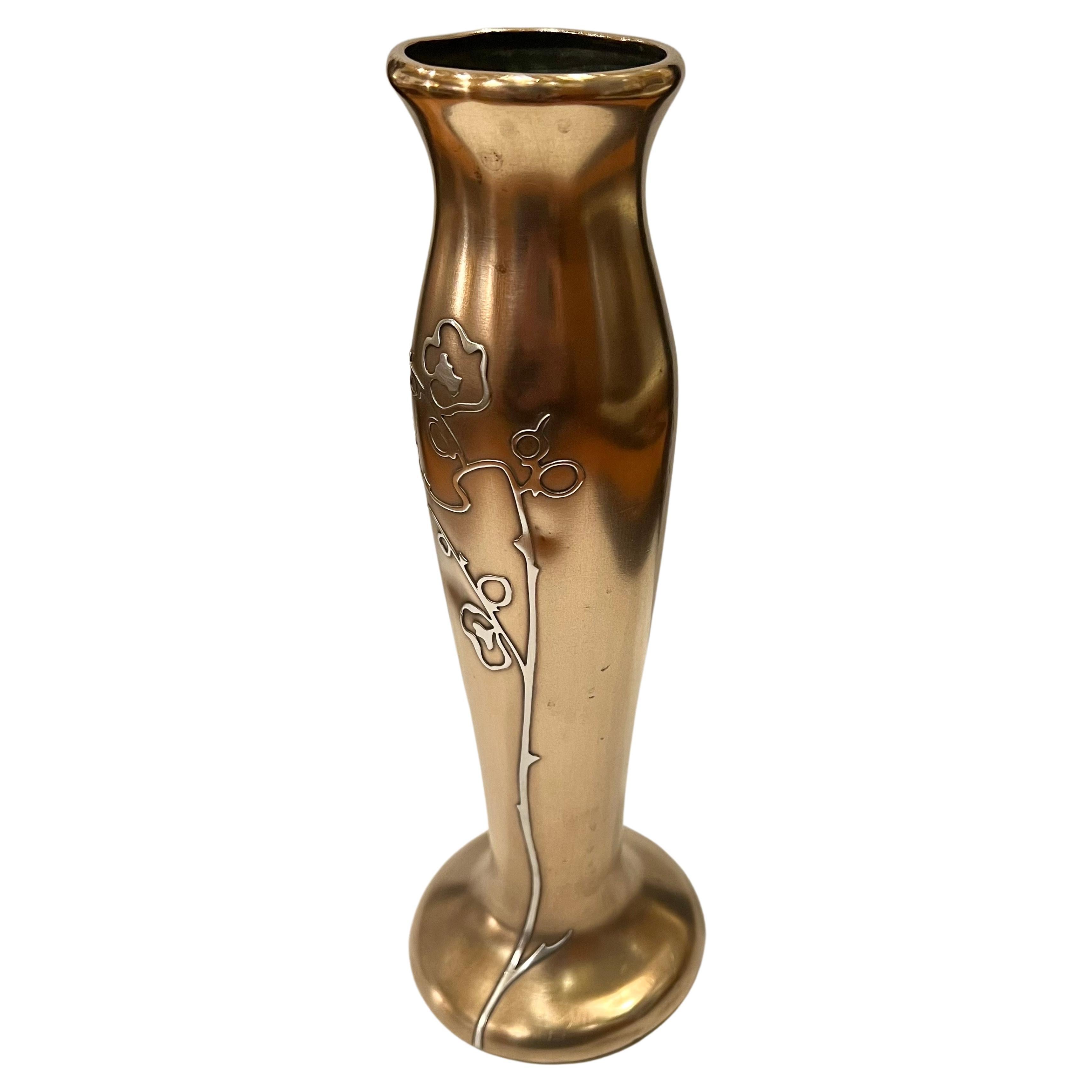 This vase was designed and handcrafted by the artisans at Heintz Art Metal Shop circa 1915. hand forged in bronze, the vase has a conical shape with a flared base and lip. A delicately articulated allium with a sinuously curved stem and leaves is