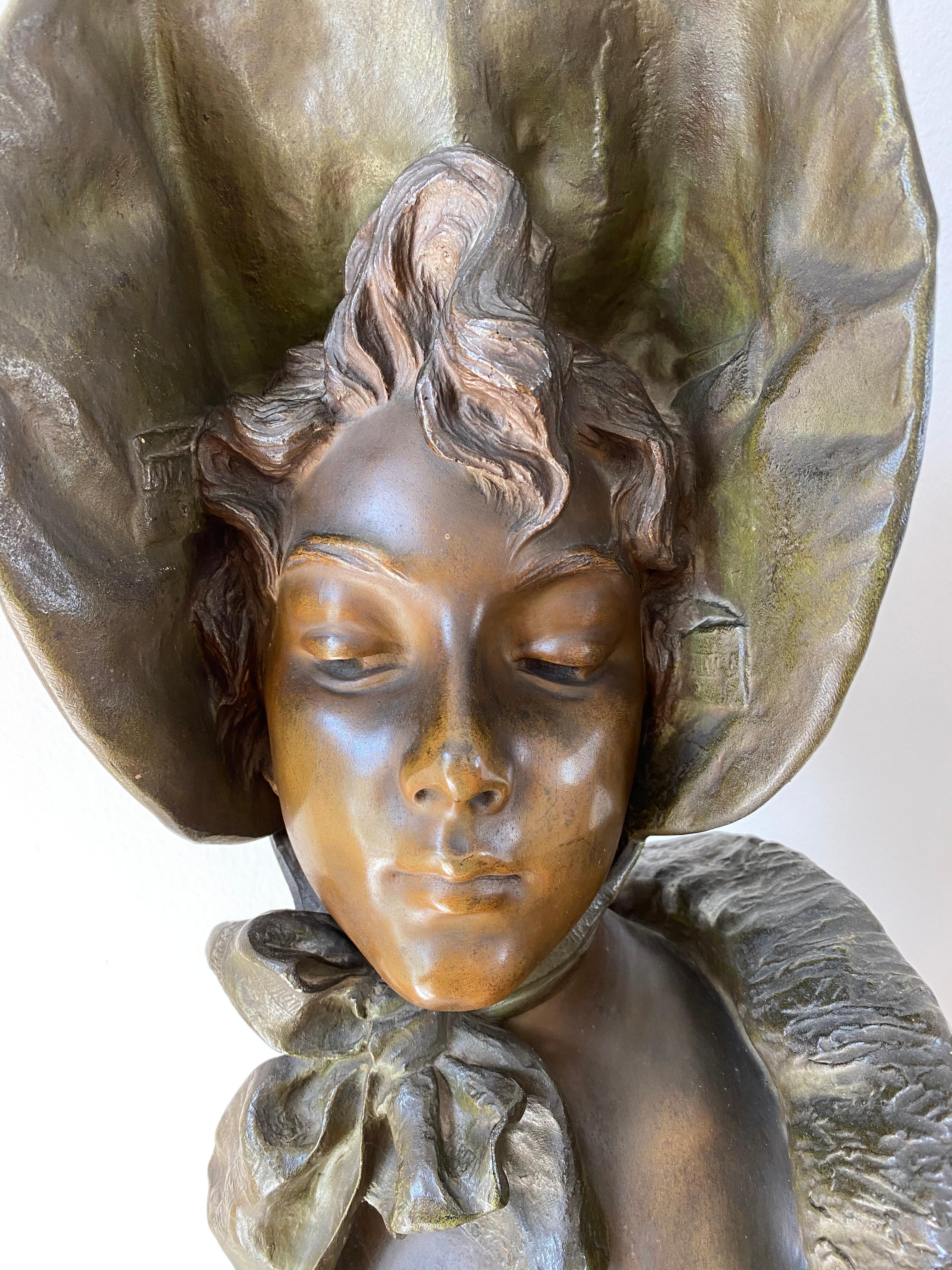 A late 19th-early 20th century French Art Nouveau bronze bust entitled “Mademoiselle Lange” of a beautiful young woman wearing a hat, modeled in the Art Nouveau style with excellent rich brown variegated patina and smooth tactile surface detail. Set
