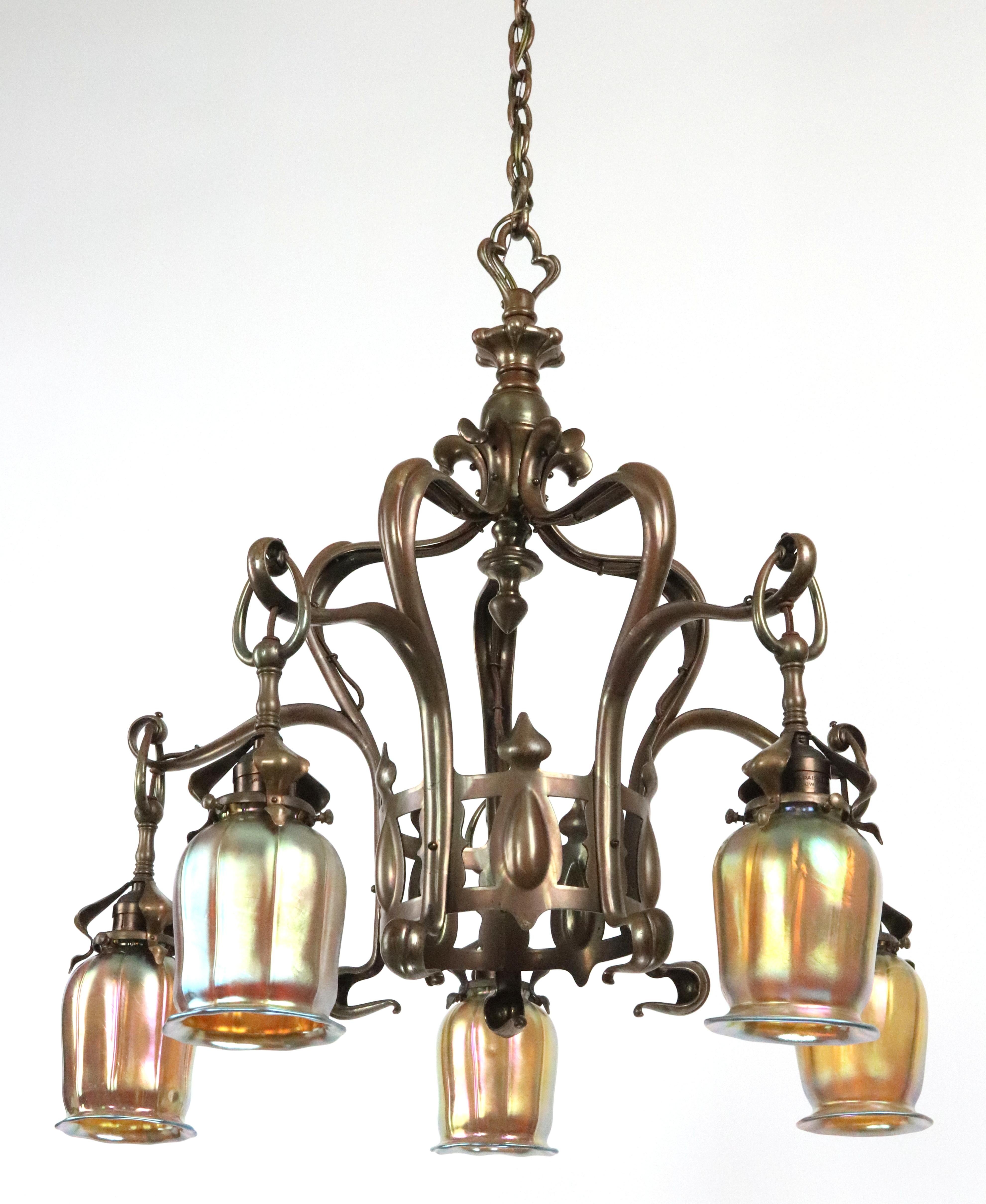 Lustre de style Arte Antiques en bronze à patine antique avec cinq abat-jours irisés orientés vers le bas. Elle nécessite cinq ampoules standard E-26 à culot moyen. Nettoyé et restauré. Bon état avec une usure appropriée due à l'âge. Cette lampe est