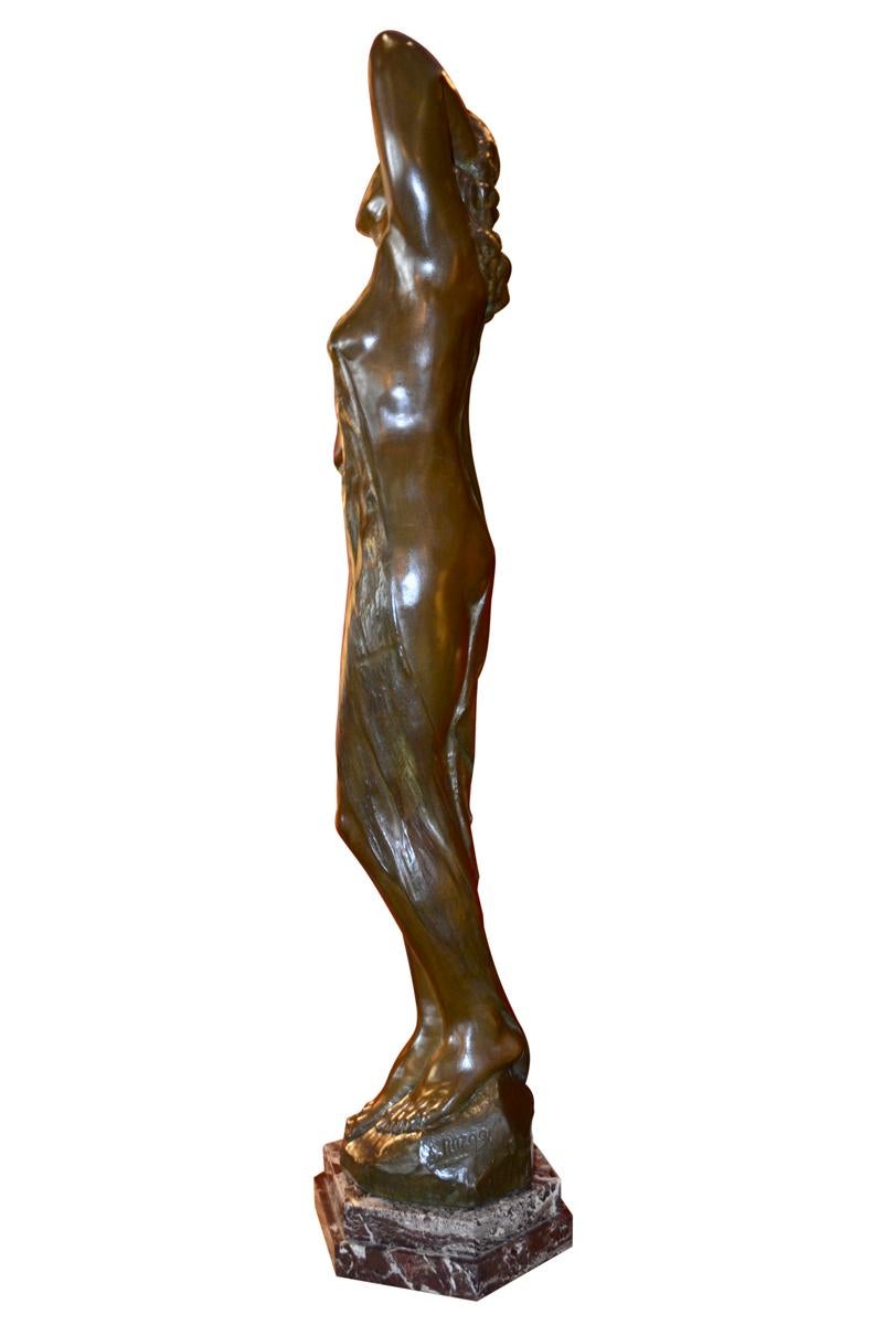 A patinated  bronze  Art Nouveau style statue of a lightly draped standing nude woman with her arms behind her head fingers run through her hair in a the manner of Rodin by Belgian Sculptor Sylvain Norga. The statue is set on an sextagonal stepped