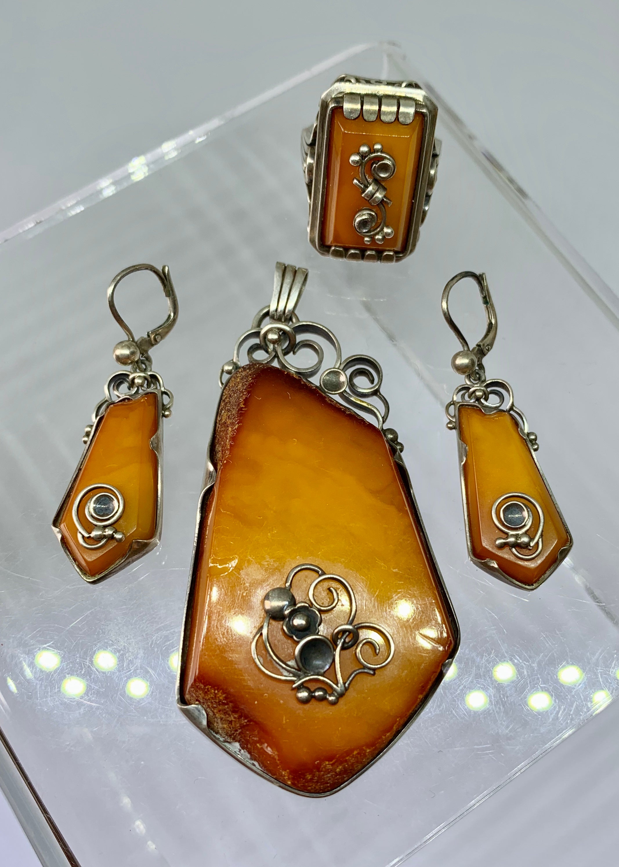 This is a magnificent Butterscotch Egg Yolk Amber and Silver suite of Pendant, Ring and Earrings.  The antique jewelry suite dates to the Art Nouveau - Art Deco to Mid-Century period.  The pieces are of extraordinary beauty and design.  The amber is