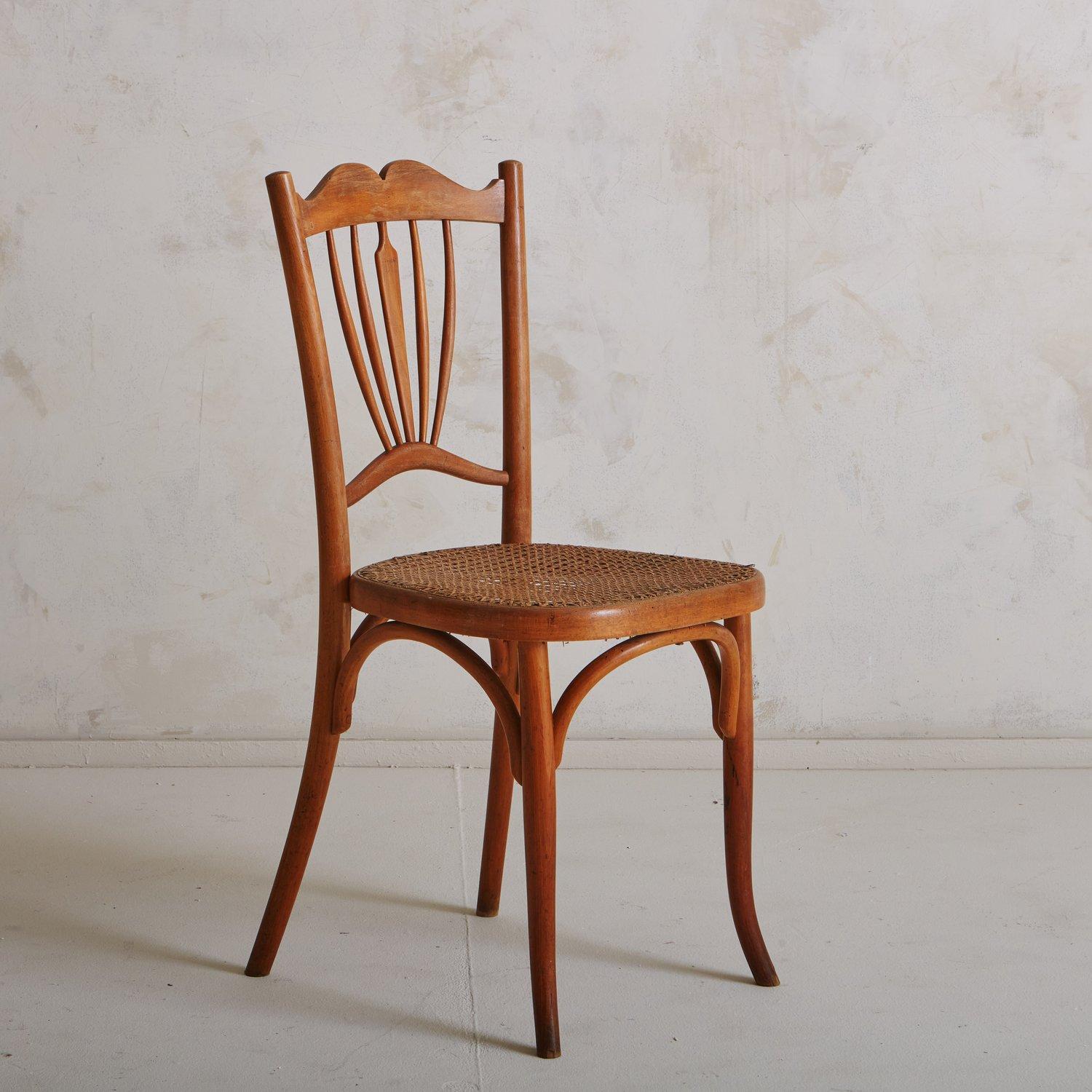 Une chaise vintage attribuée à Fischel avec un cadre en bois sculpté, un dossier décoratif complexe et une assise en rotin. Cette pièce est documentée dans le catalogue Fischel n° 150. Provenance : France, début des années 1900.

