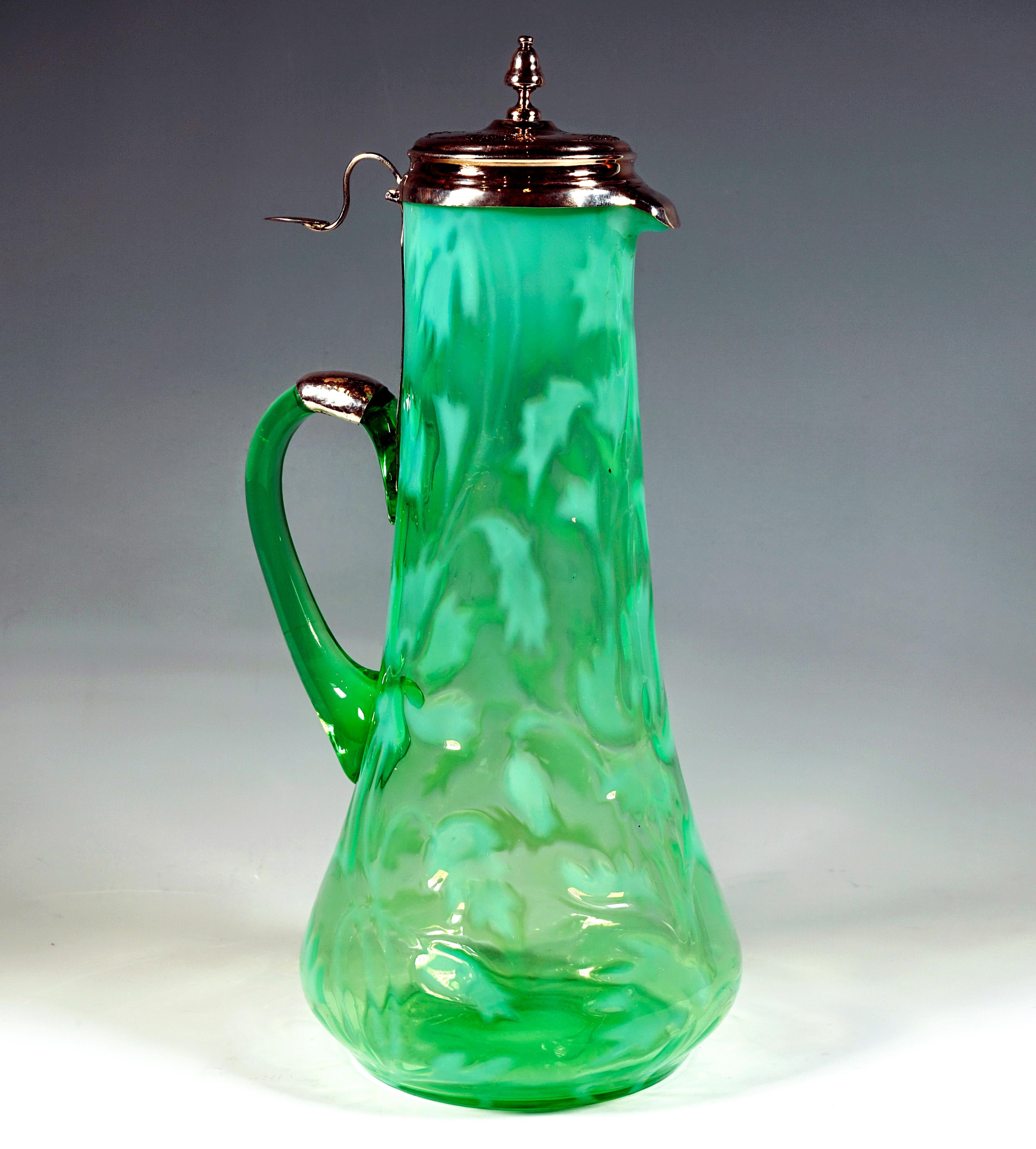 Carafe made of green glass with cryolite inclusions (opaline) in the shape of feathered leaves, with a conical body that swings out slightly at the bottom on a round, flush stand, beak spout, opposite attached glass handle, silver fittings above the