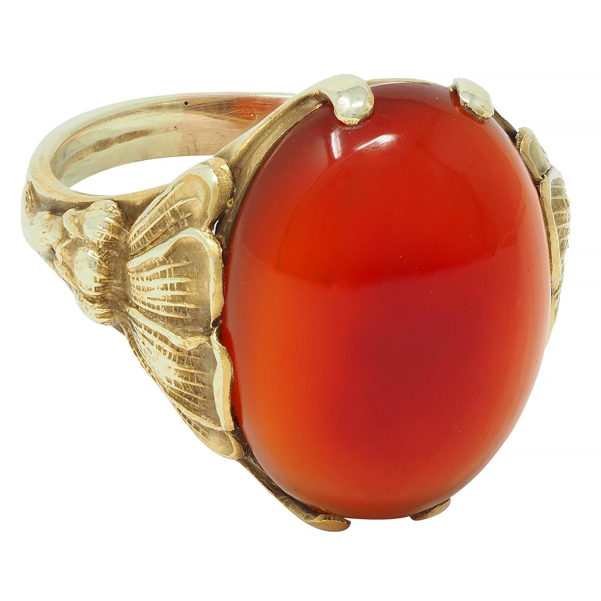 Centering an oval-shaped carnelian cabochon measuring 12.0 x 16.0 mm 
Translucent orangey red in color with medium saturation 
Prong set and flanked by highly rendered shoulders
Depicting stylized poppy flowers with engraved texture
Stamped for 14