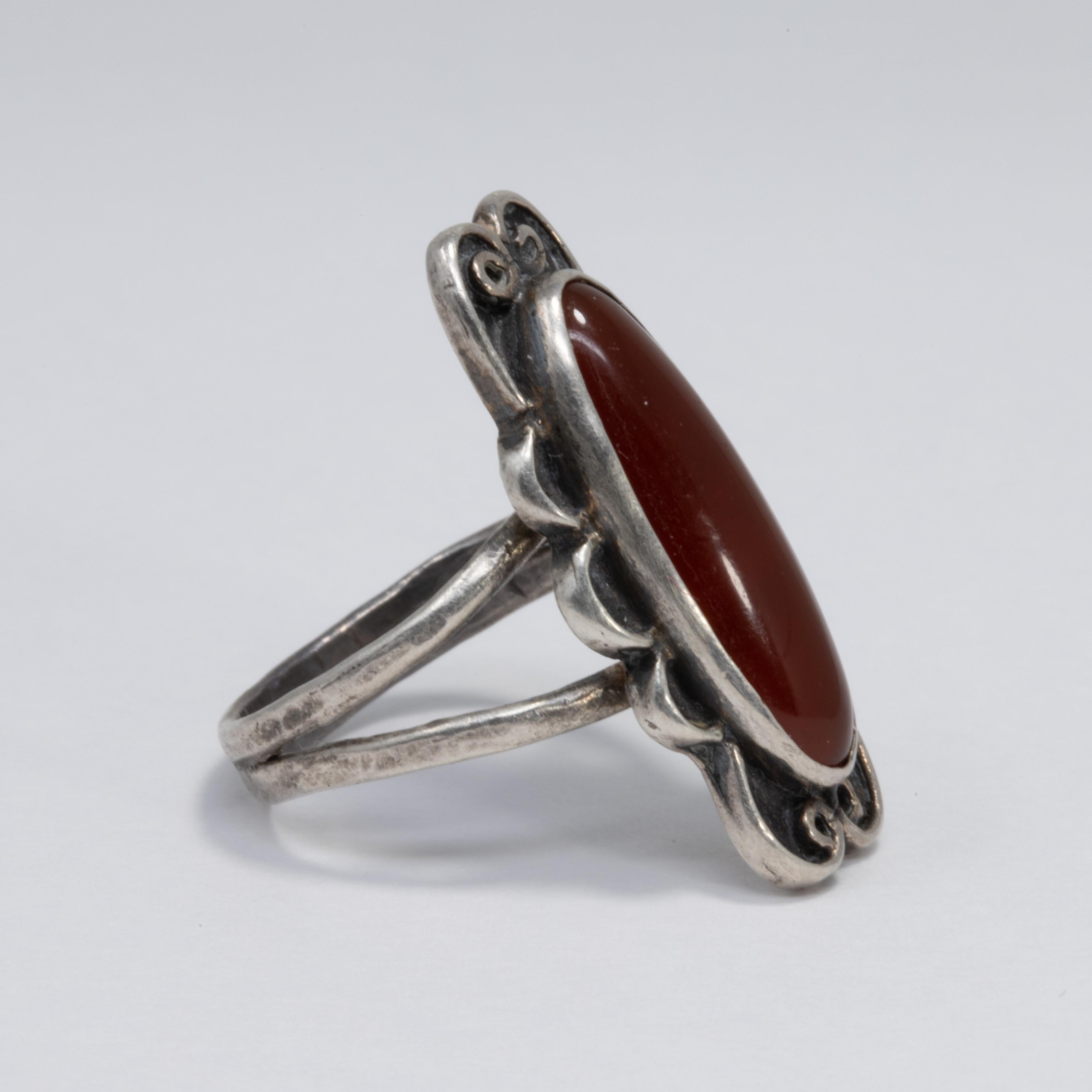 Ein exquisiter Jugendstil-Ring mit einem Karneol-Cabochon als Herzstück. Dekorative Lünette und Band aus Sterlingsilber.

Ringgröße US 7.75

Zeichen / Punzierungen / etc: Sterling