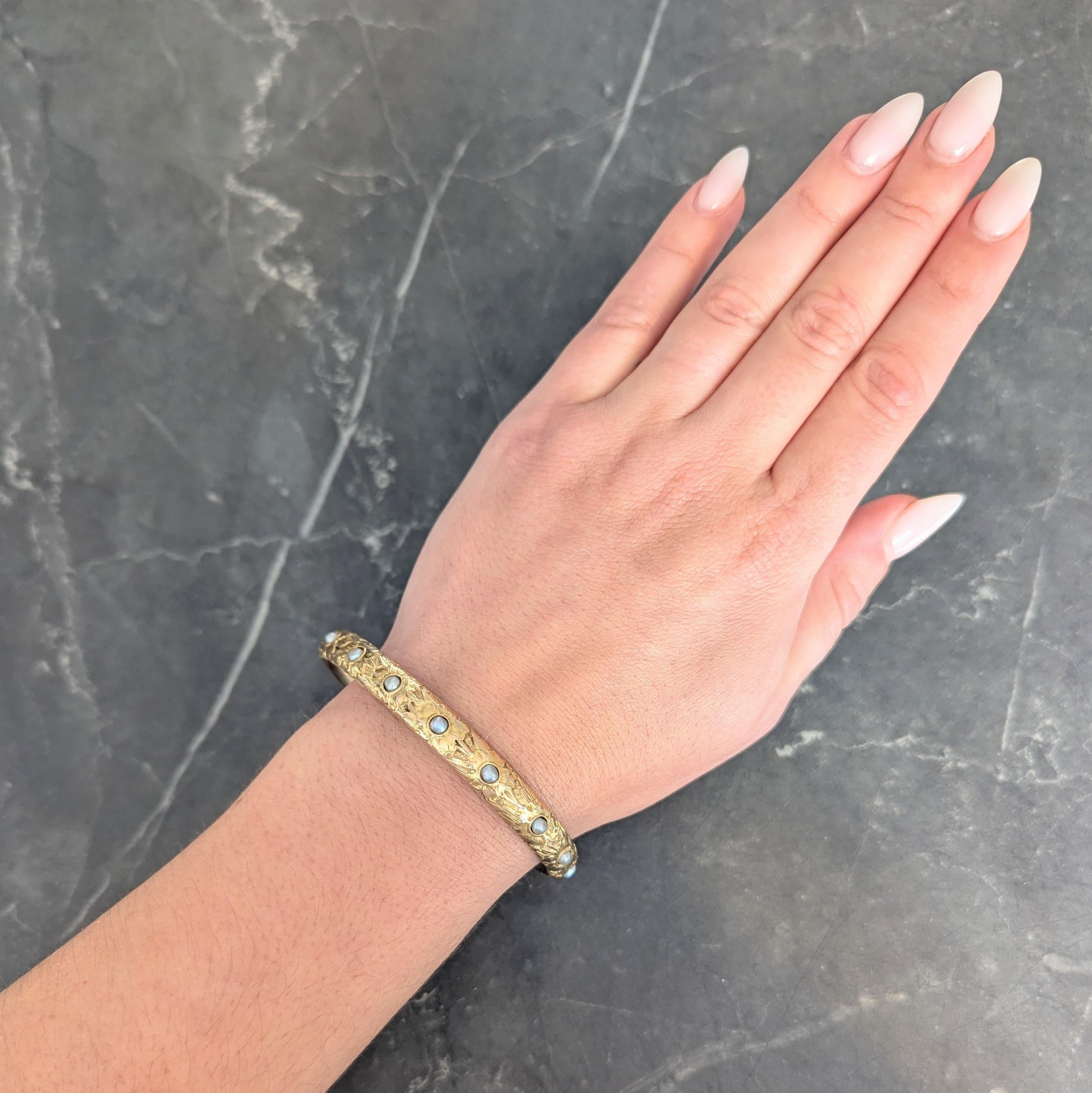 Designed as an oval shaped bangle with floral motif fully around
Raised with engraved detailing and each centering a pearl
Measuring 3.0 mm near-round - gray in body color
Exhibiting strong iridescence and bezel set
Stamped for 14 karat gold
With