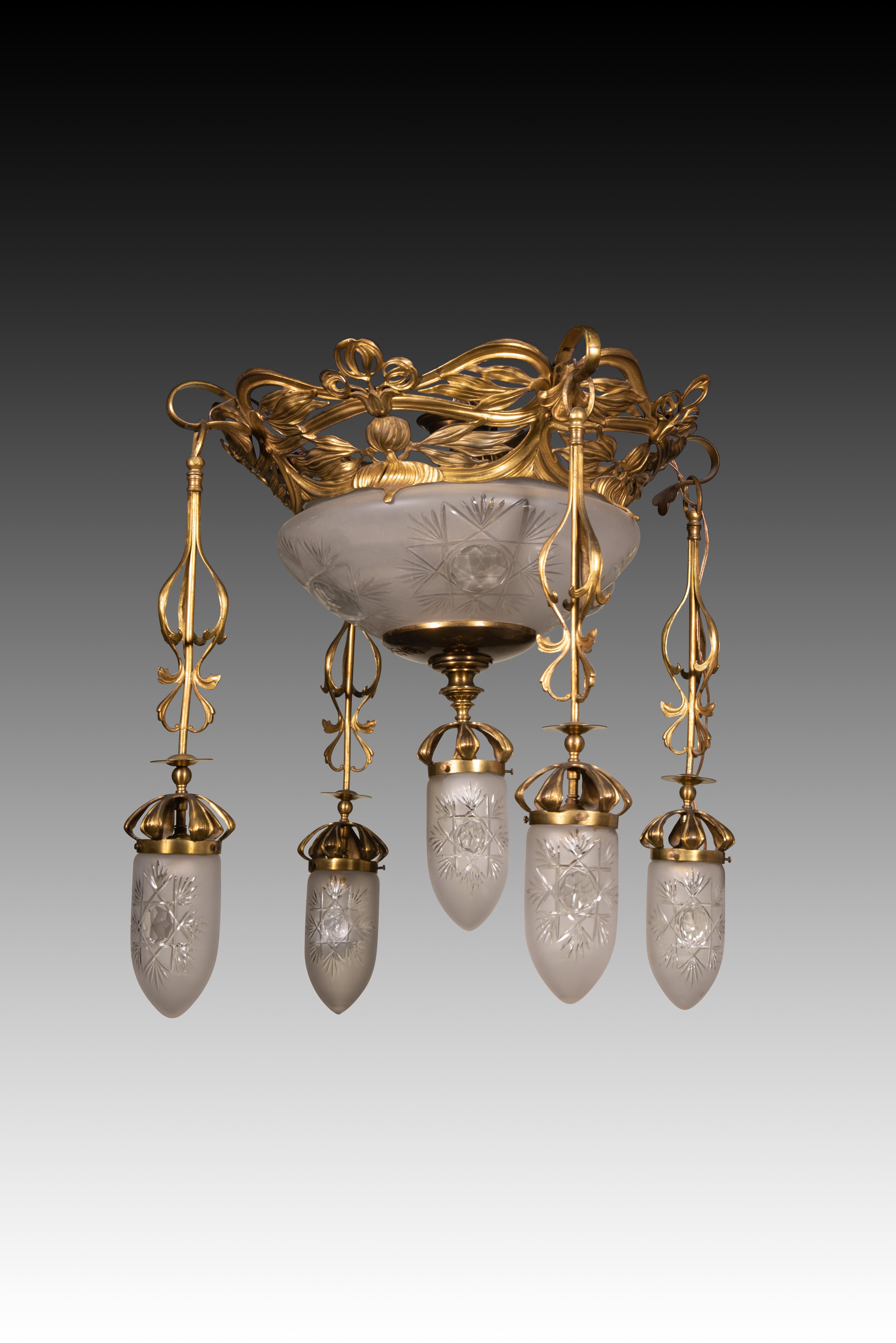  Lampada da soffitto in stile Art Nouveau. Metallo, vetro. Circa 1900.
 Lampada da soffitto in metallo dorato con diversi punti luce nascosti da paralumi in vetro traslucido bianco decorati con elementi geometrici. I gambi, le foglie e le forme che