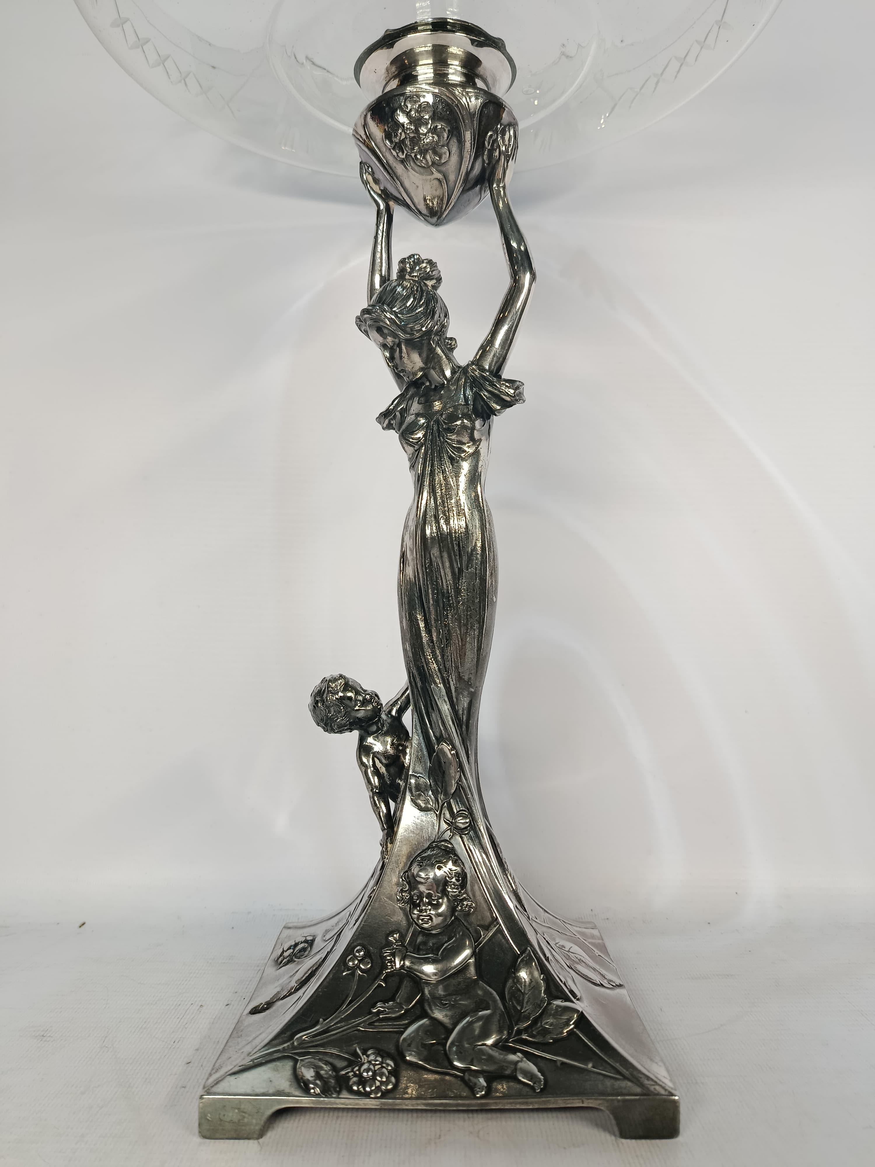 Exquise pièce centrale Art nouveau réalisée par WMF (Württembergische Metallwarenfabrik), l'un des fabricants allemands les plus renommés d'objets décoratifs en métal au début du XXe siècle. Cette élégante pièce est fabriquée en métal blanc avec une