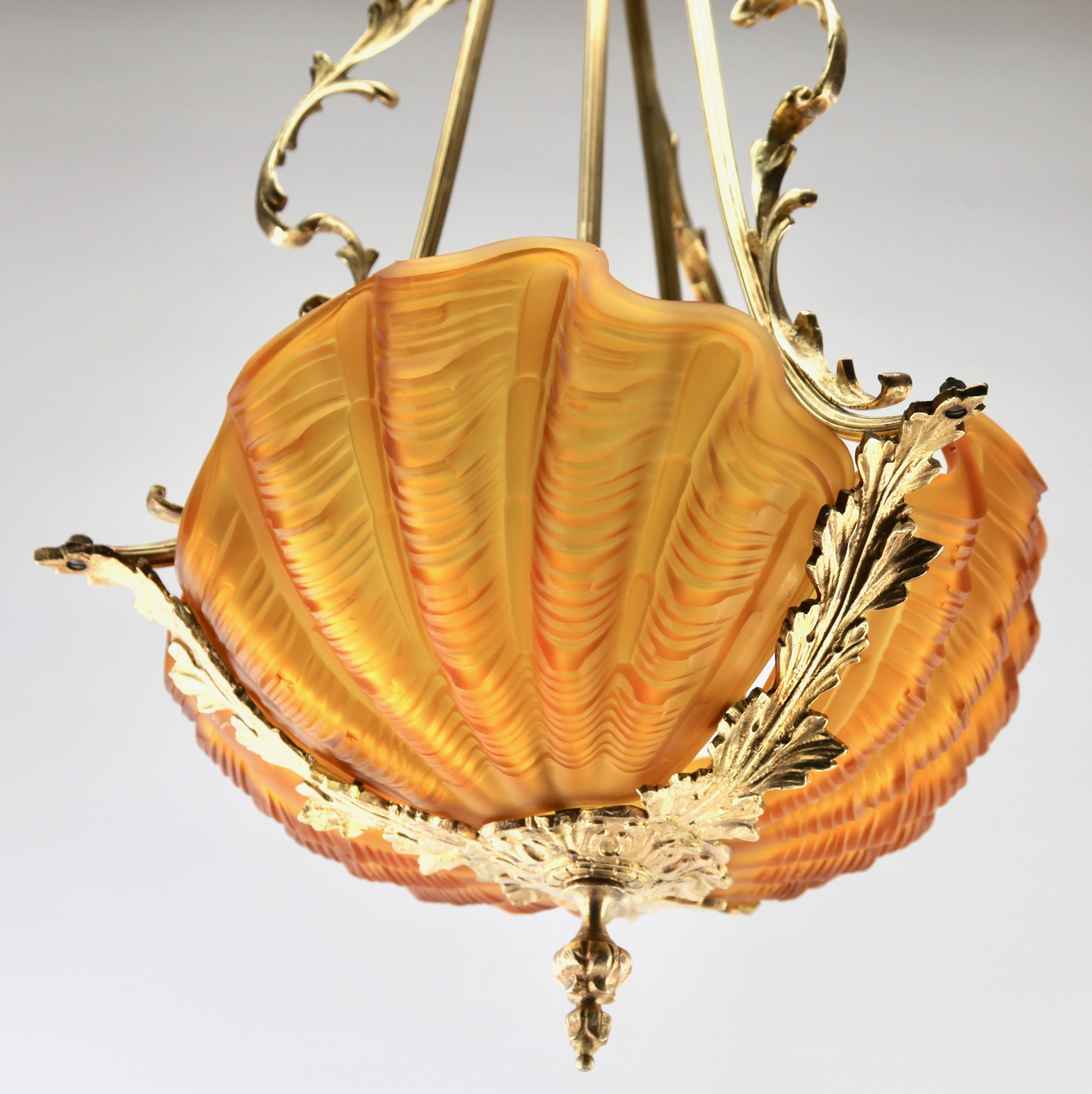 Three clam shells suspended between fronds of seaweed.
The shade is cast in pink opaque glass enhancing the shadow of the shell’s texture, and they are held in naturalistic framework of polished brass rococo scrolls representing fronds of