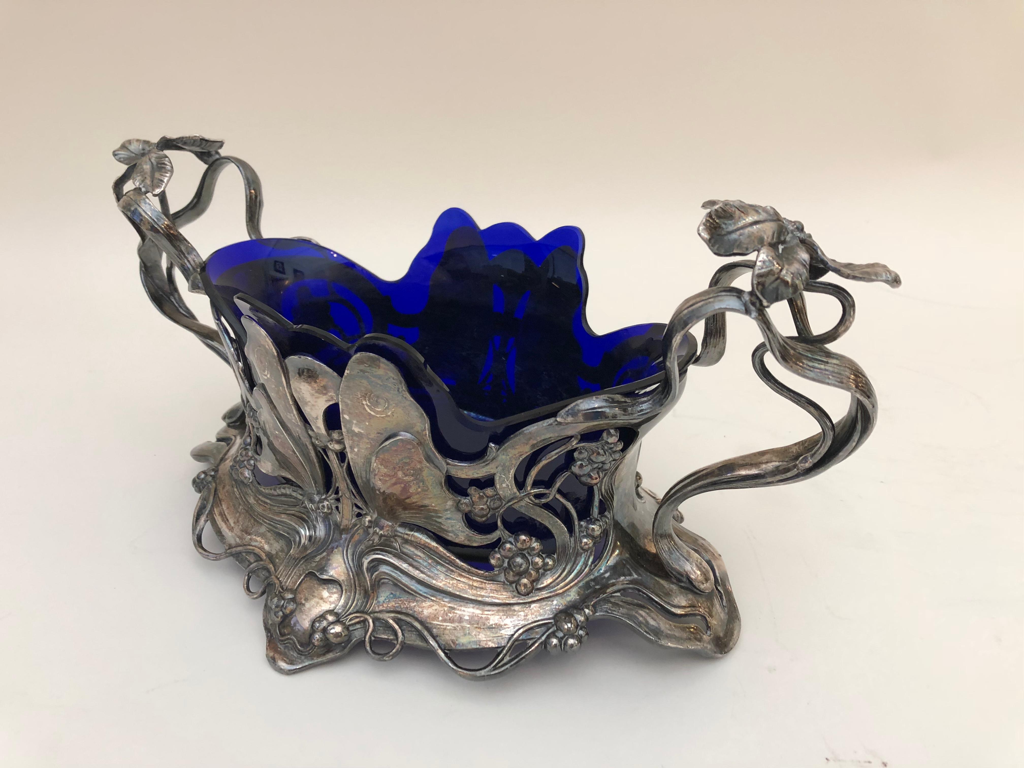 This ravishing Art Nouveau silver plated centrepiece is decorated with butterflies, flowers, and budding tendrils, and retains the original applied patina and cobalt-blue-glass liner. Designed by the German sculptor Albert Meyer, it bears the stamp
