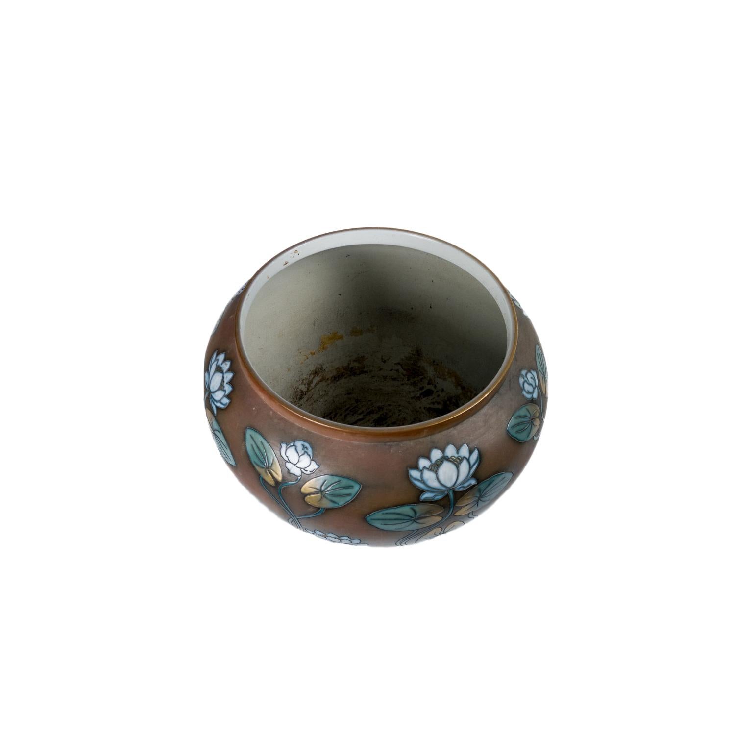 A rounded Art Nouveau ceramic plant pot dates from the early 20th century, produced in the renowned French factory Sarreguemines and features a striking lotus flower motif in soft enamel relief. The body is finished in a warm brown glaze, against