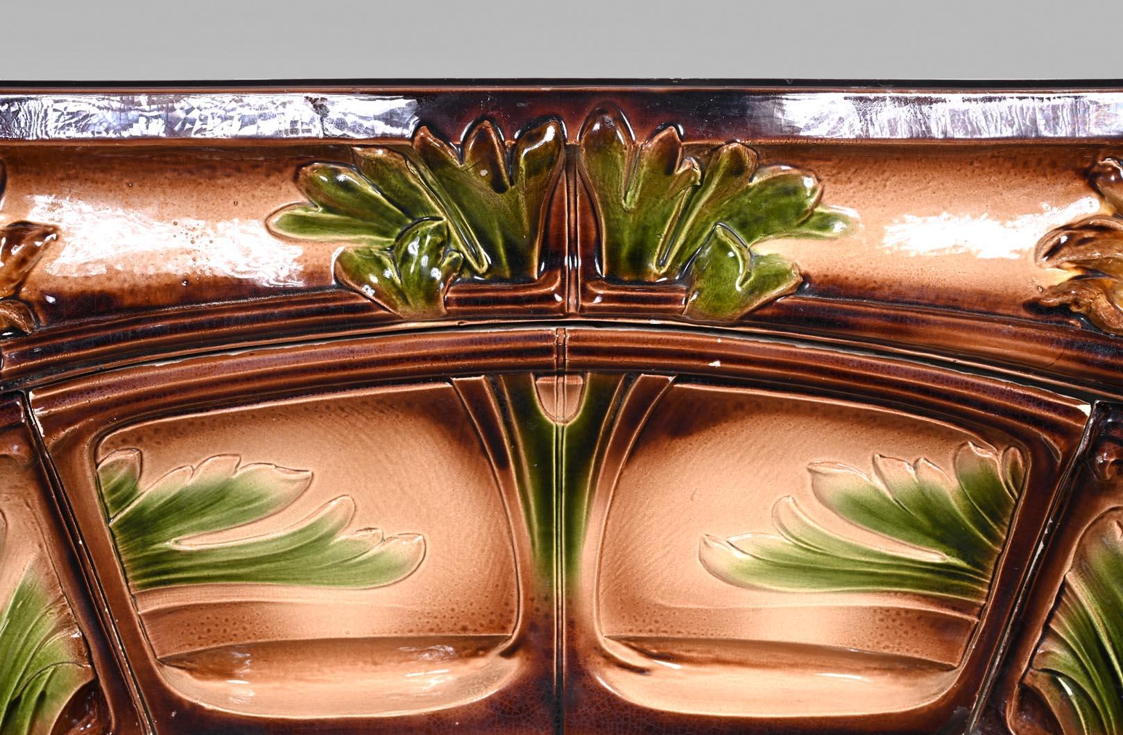 A rare polychrome glazed ceramic fireplace crafted by the MANUFACTURE DE VITRY-LE-FRANÇOIS, circa 1900. This striking Art Nouveau piece features a richly detailed relief decoration of stylized sunflowers and foliage, rendered in a harmonious palette