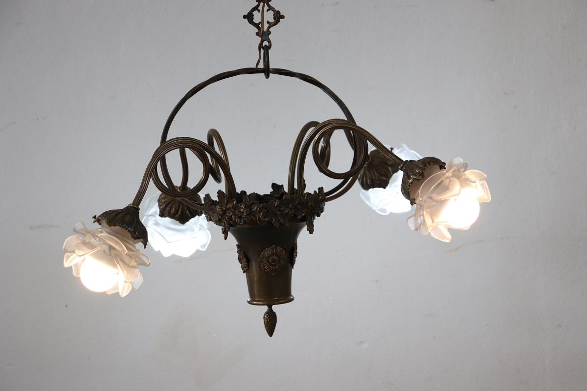 Beautiful and refined Italian 1910s of the period Art Nouveau chandelier with 4 bulbs. The chandelier is made of burnished brass. Characterized by a particular basket shape from which curled arms branch off and end in flower-shaped glass bowls with