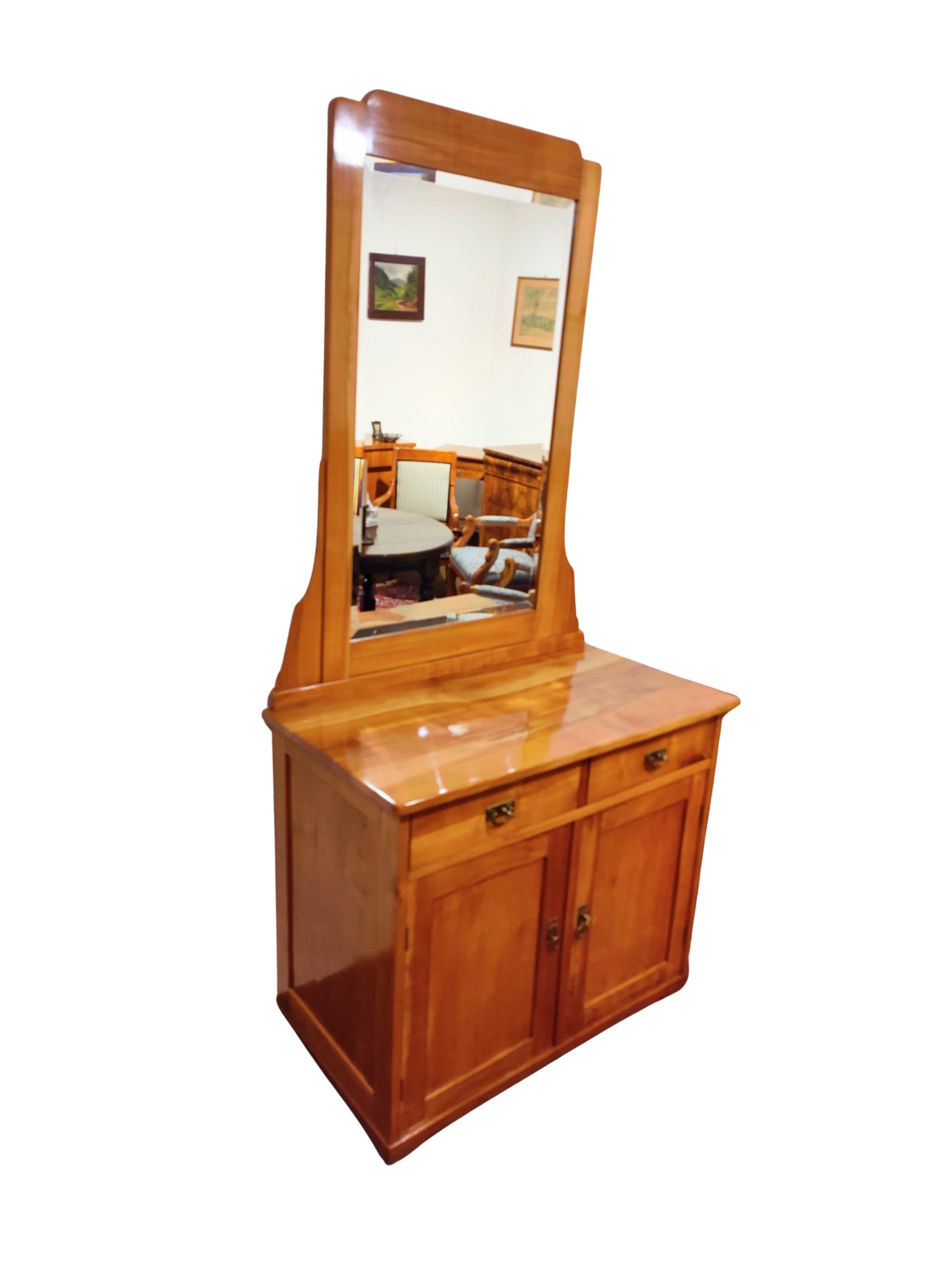 Elegant Art Nouveau cabinet crafted from solid cherrywood, South Germany circa 1905.
The piece features a tall, slightly forward-leaning mirror with beautifully facetted edges – a characteristic detail of the period. Beneath the mirror, two drawers