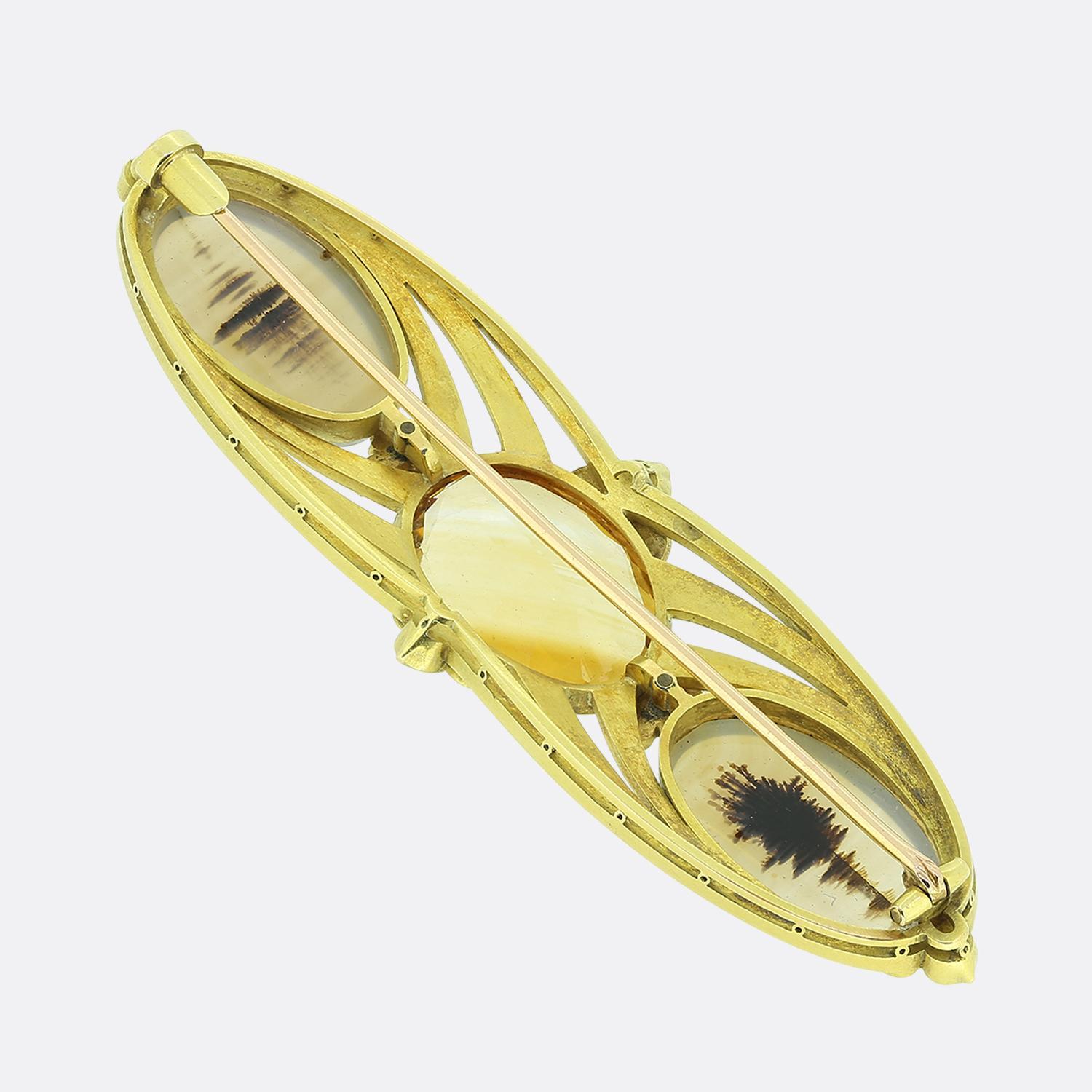 Hier haben wir eine stilvolle Brosche mit einem auffälligen Design, das einen orangefarbenen Citrin in der Mitte zeigt, der von zwei Achatsteinen flankiert wird. Der Rahmen ist komplett aus 18 Karat Gelbgold gefertigt und wird durch zarte