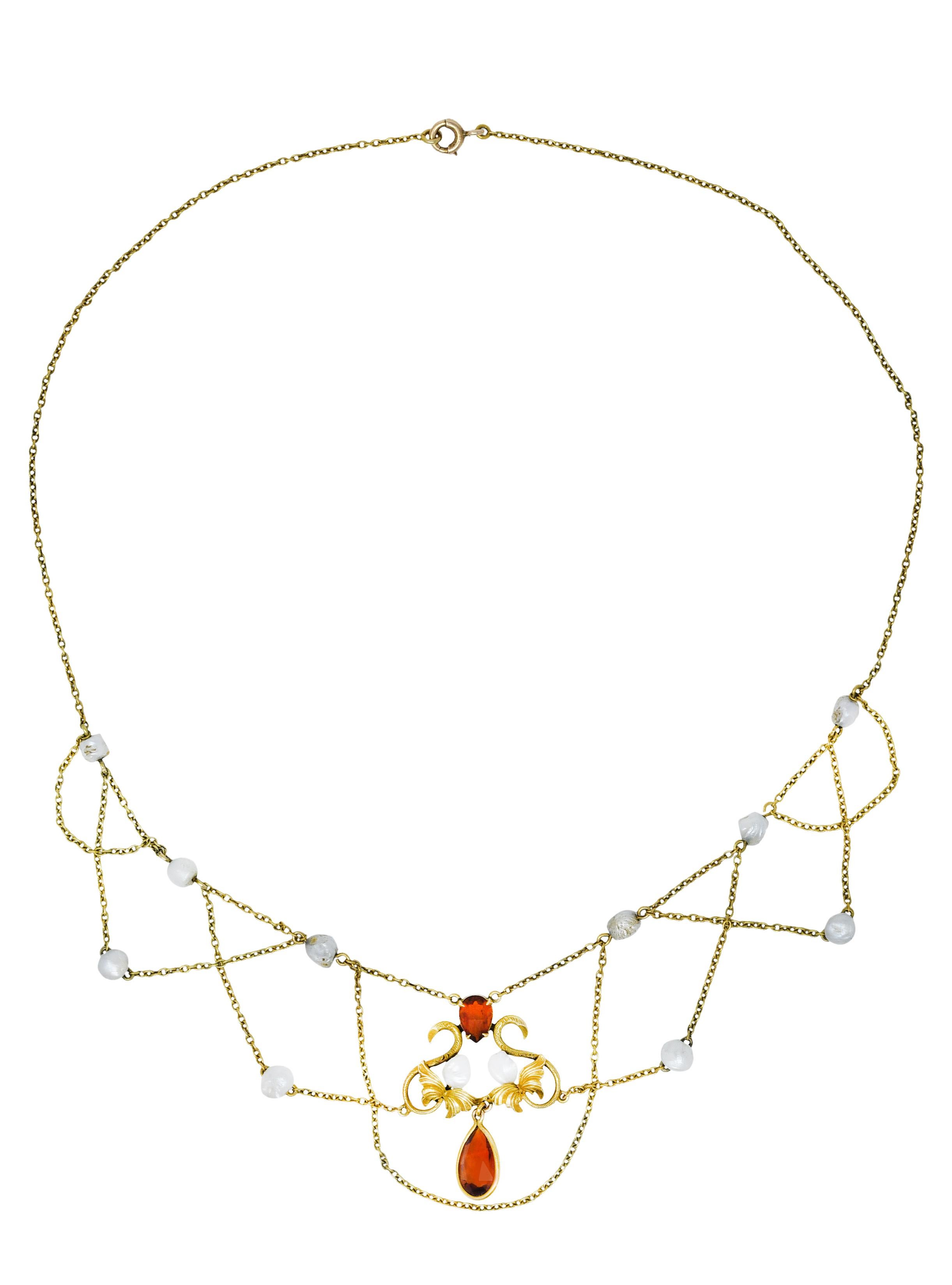 Cable chain necklace features swagged chain accented by baroque pearl stations

Measuring approximately 4.5 mm - white in body color with moderate to strong iridescence

With a scrolling central station designed with whiplashed foliate and two pear