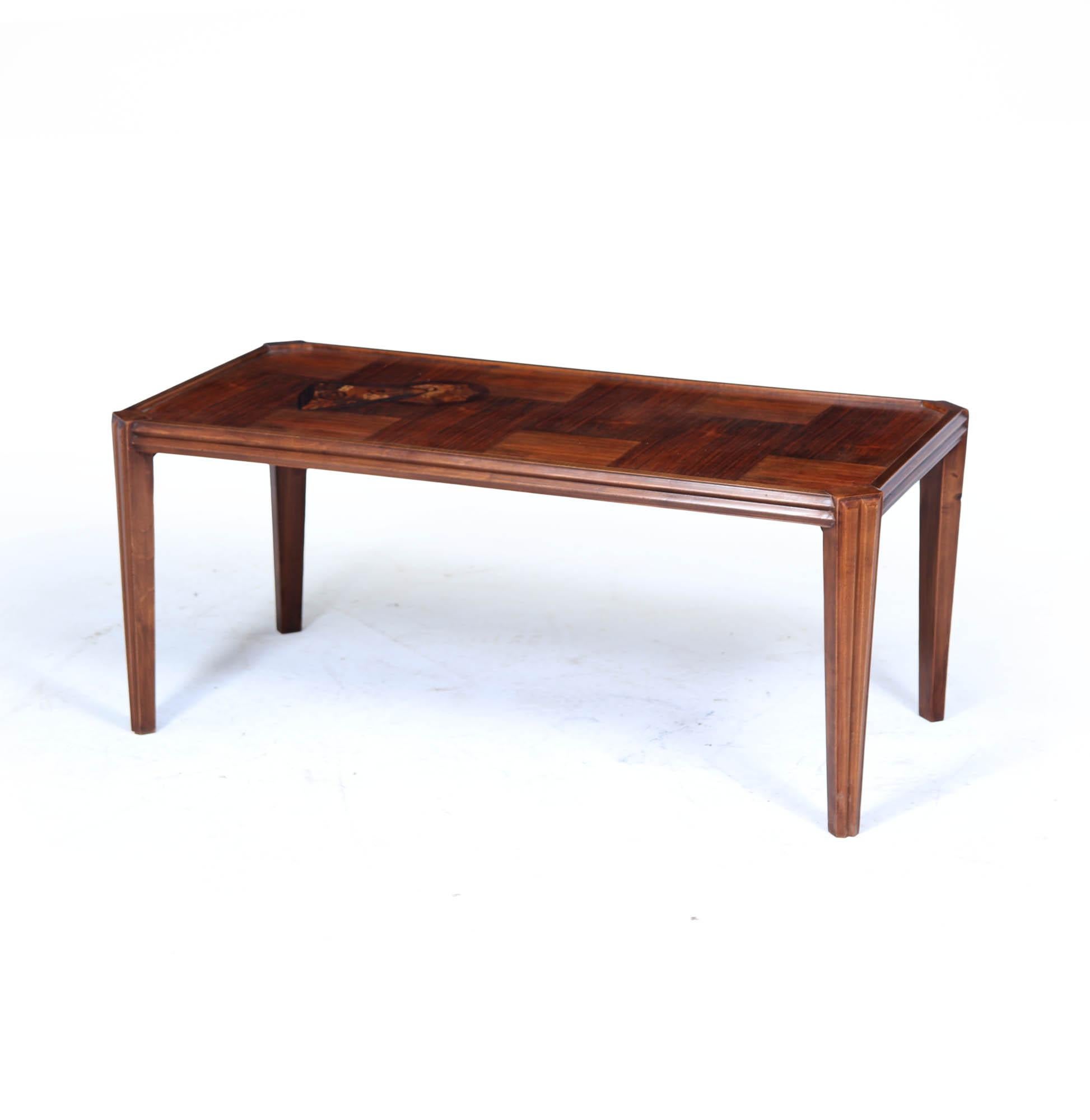 A finely crafted and characterful table from the School of Nancy, showcasing the artistry of French decorative arts in the early 20th century. Made in Indian rosewood and mahogany, the table features a striking inlaid motif to the top and is signed