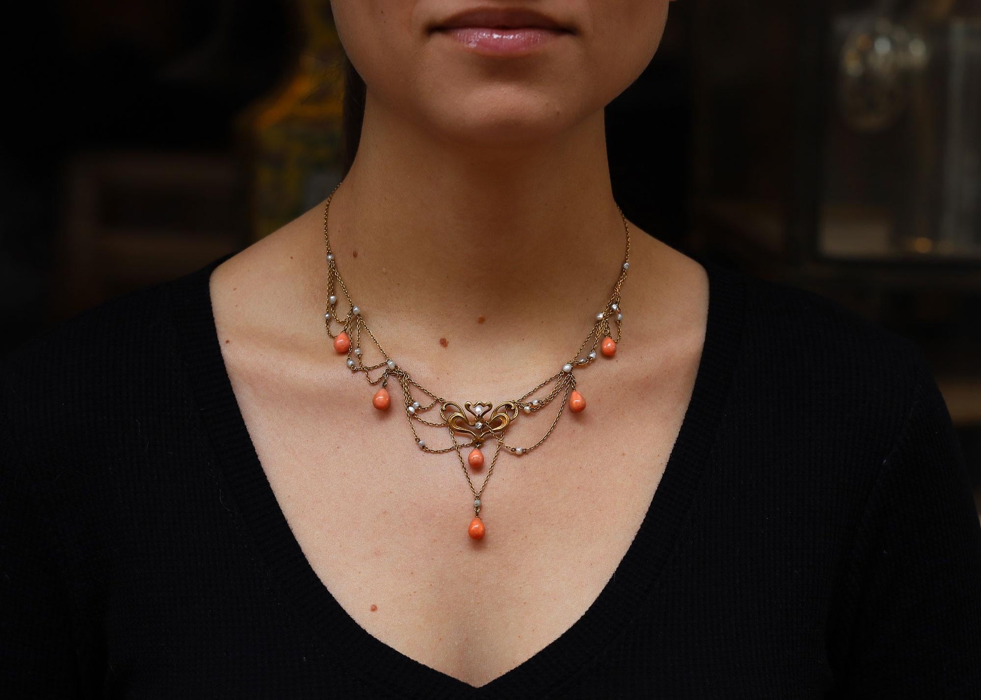 The Hudson Court Art Nouveau swag necklace dates to the early 1900s and is adorned with a swirling central plaque and stations of pastel peach coral and natural seed pearls. Also known as a festoon bib necklace, this authentic antique treasure oozes