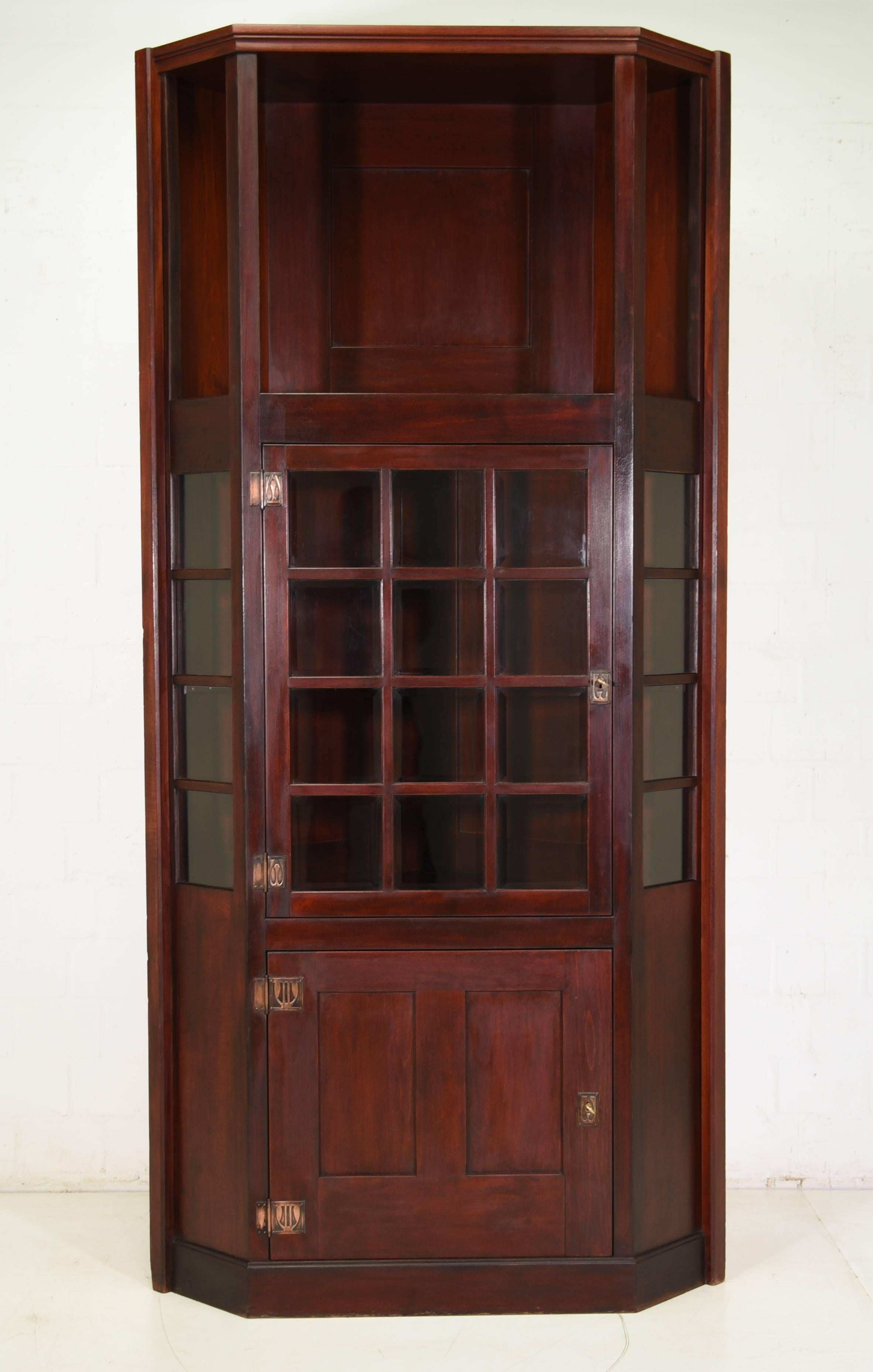 An Art Nouveau corner cupboard from circa 1915 in mahogany colors. The corpus is completely made of solid wood mostly of birch with oak accentuations. The fittings, locks and keys are originals from the manufacture and still work. The center has a