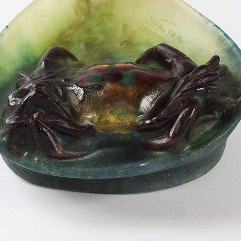 Une Crabe française, pâte de verre vide-poche par Amalric Walter. Le crabe brun-rouge a des taches vert foncé, rouges et jaunes sur la partie supérieure de sa carapace. Il est assis sur une vague verte avec de longs fils d'algues, vers 1920.

Un