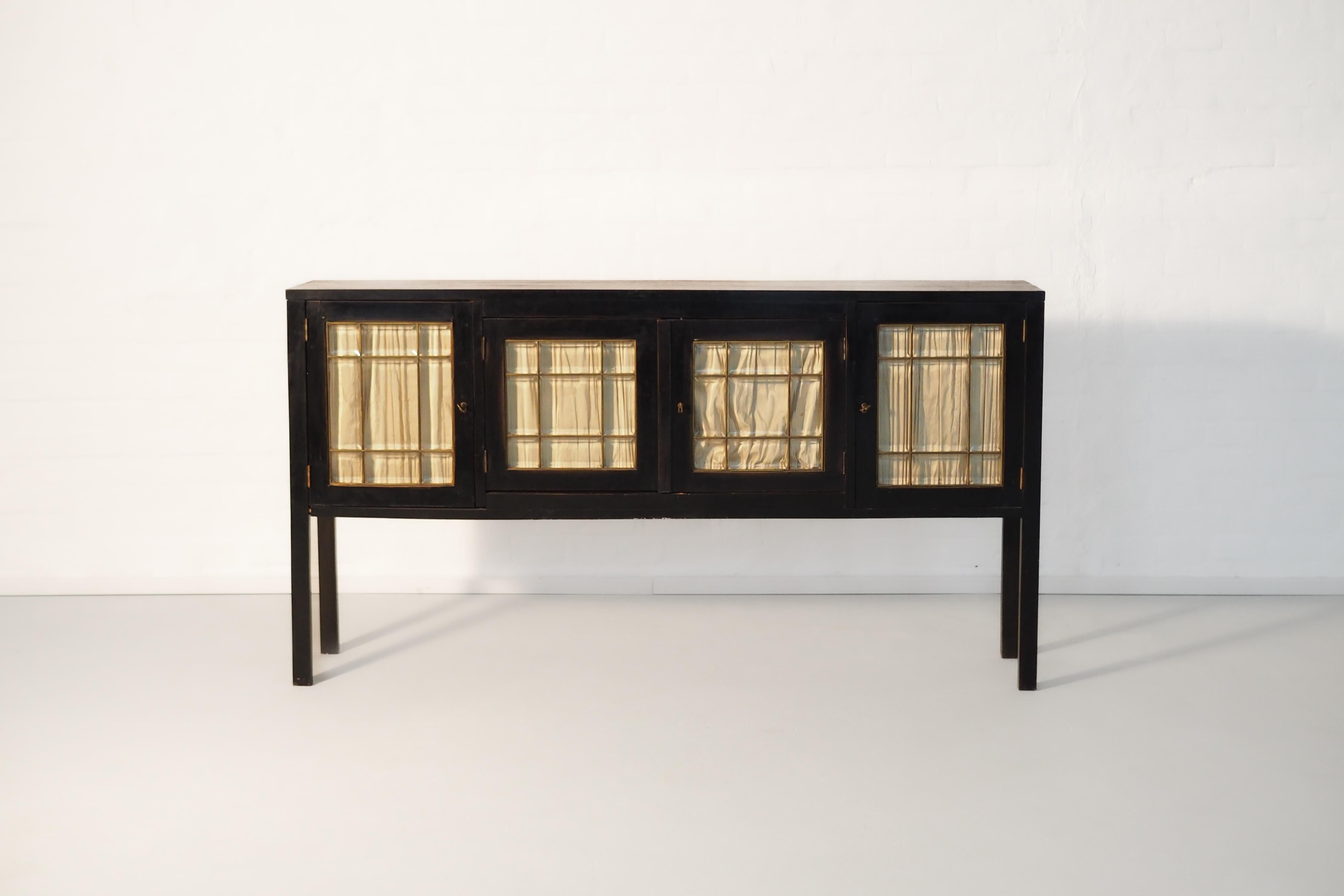 Questa eccezionale vetrina in stile Art Nouveau incarna una maestria artigianale e un'eleganza senza tempo. La sottile struttura in legno nero emana un'estetica raffinata, mentre le quattro ante in vetro sono caratterizzate da un delicato supporto