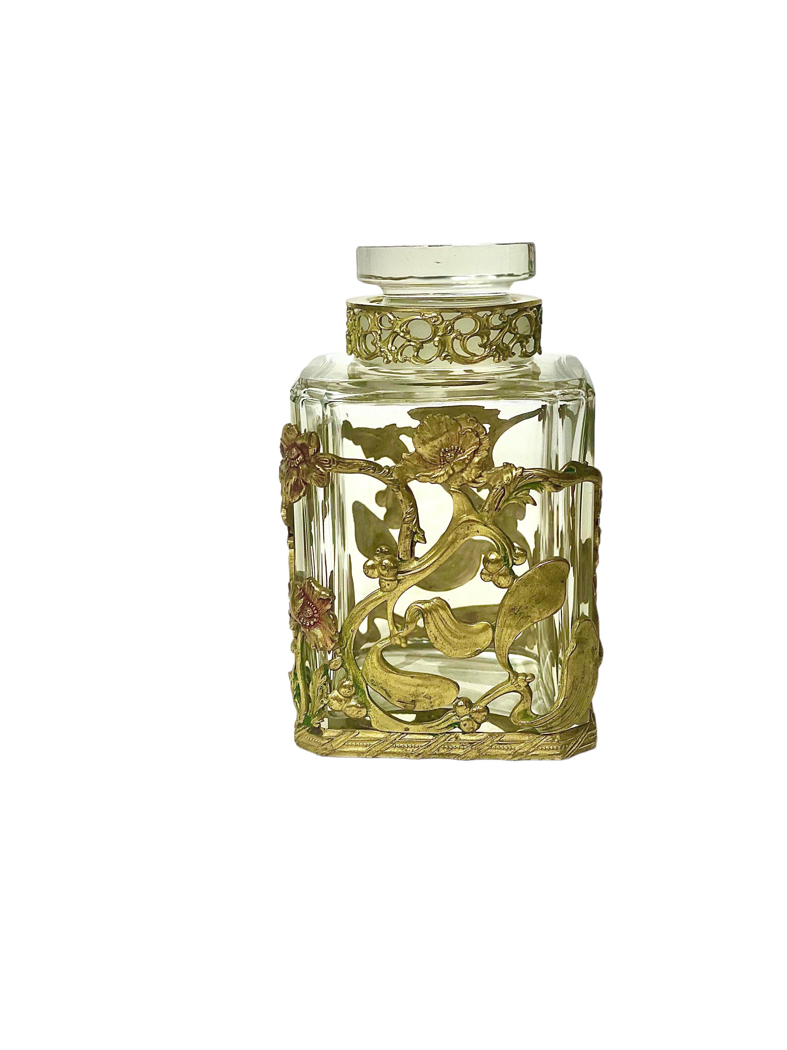 A pretty crystal, stoppered bottle, intricately clad in an openwork gilt-brass motif of entwined poppies and mistletoe. This square-sided Art Nouveau period bottle features a simple, but elegant flattened, cylindrical crystal stopper. There is a