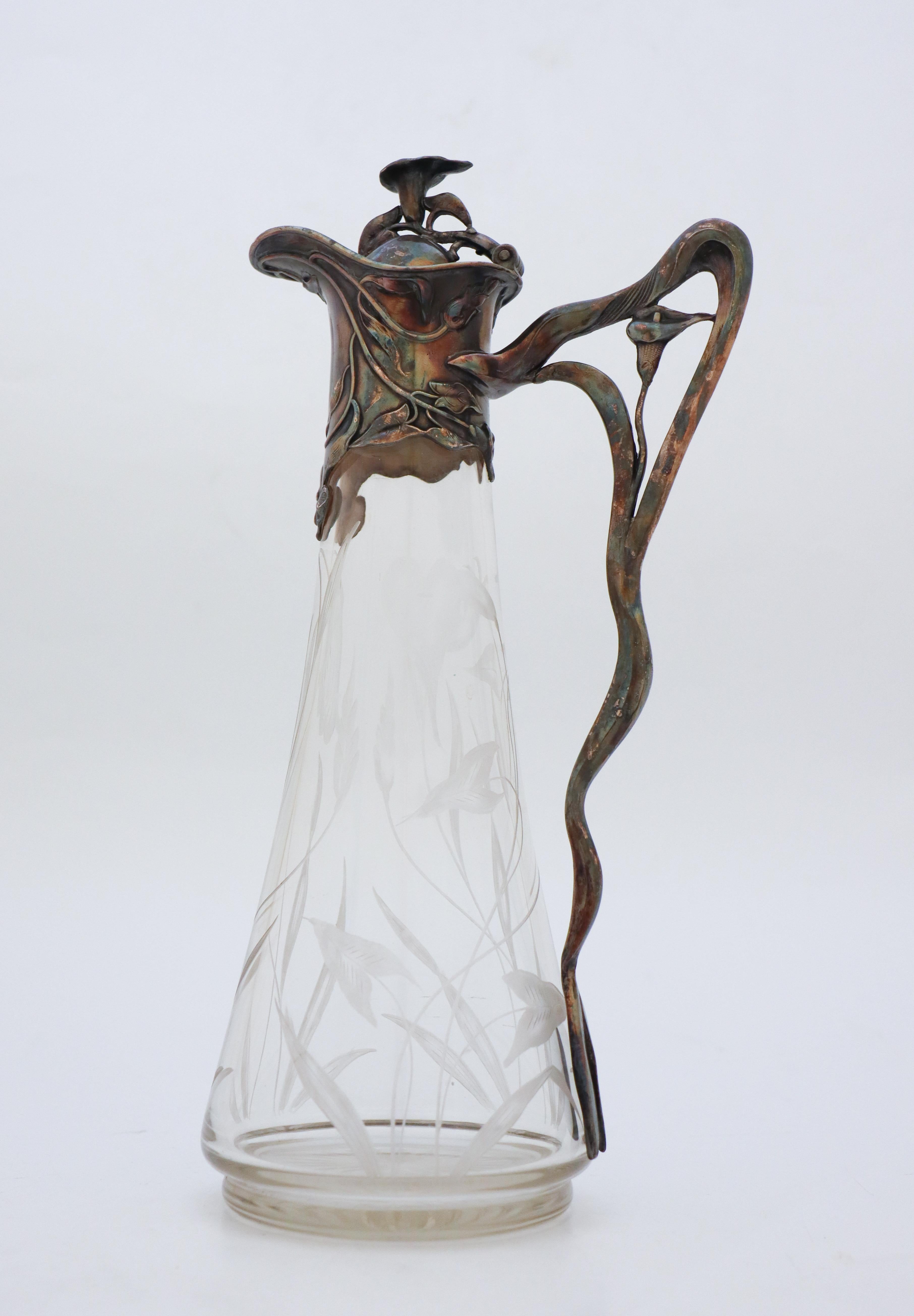 A decanter in Art Nouveau-style. Engraved floral decor on the glass and a lovely art nouveau shape on the metal. It is probably designed in Germany in the early 20th century. It is 32 cm (12,8