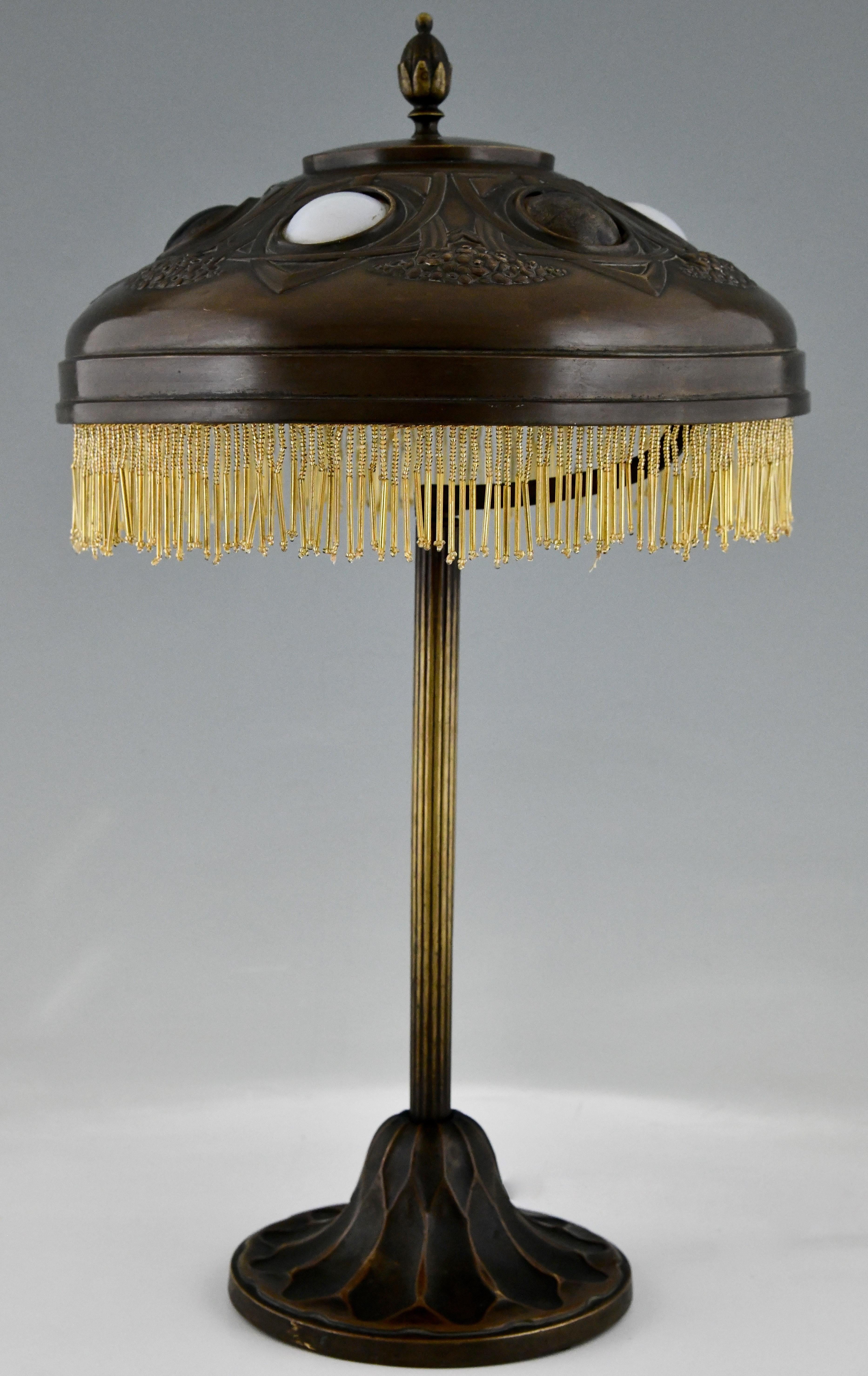 Lampe de bureau Art nouveau en bronze patiné avec abat-jour en laiton martelé et incrustation de verre.  
Des fioritures jaunes et dorées. France ca. 1900