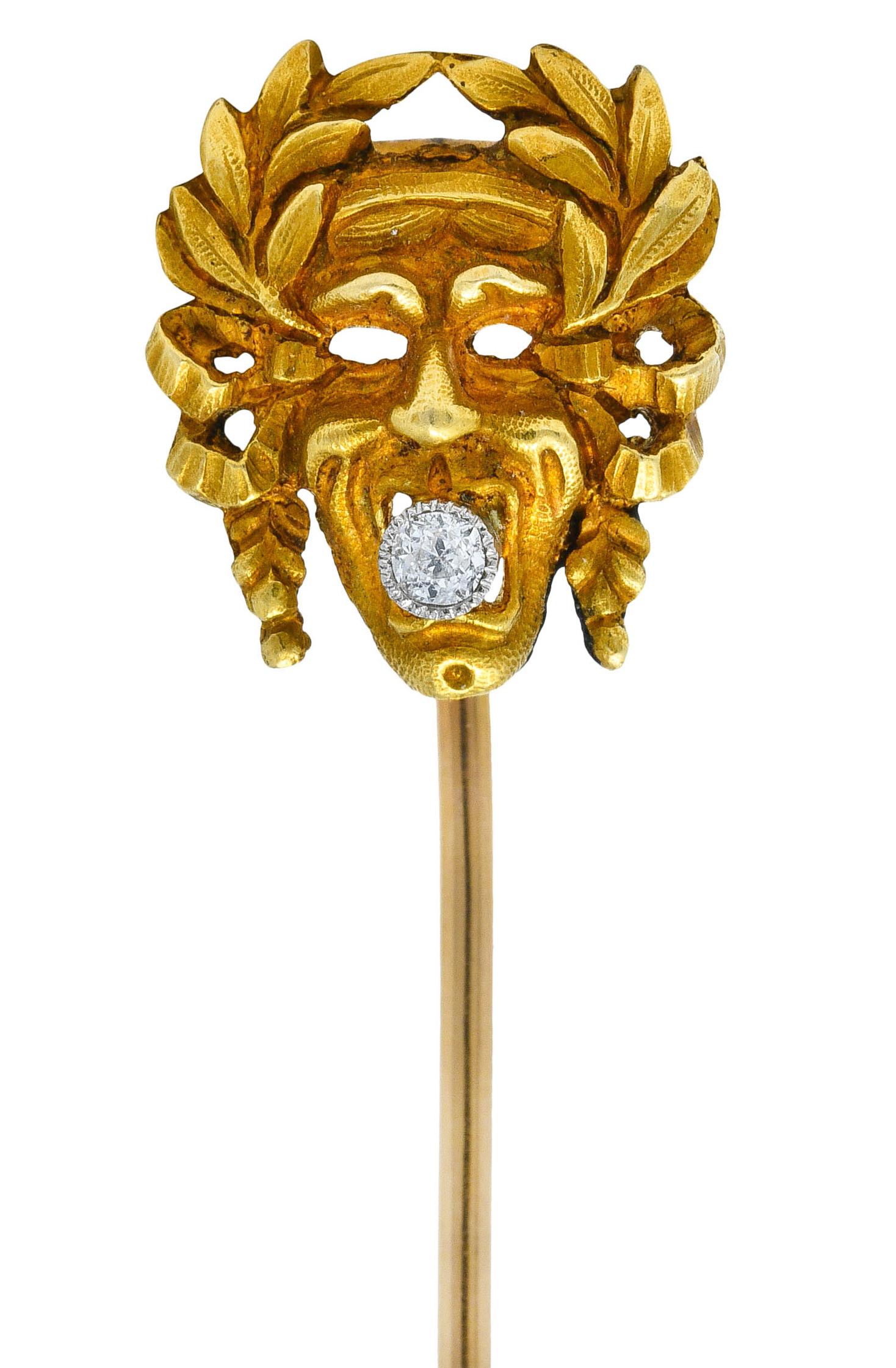 Depicting a stylized comedy mask adorned with a ribboned crown of laurels

Clutching an old European cut diamond in its mouth

Bezel set in platinum while weighing approximately 0.05 carat - eye clean and white

Tested as 18 karat gold

Circa: