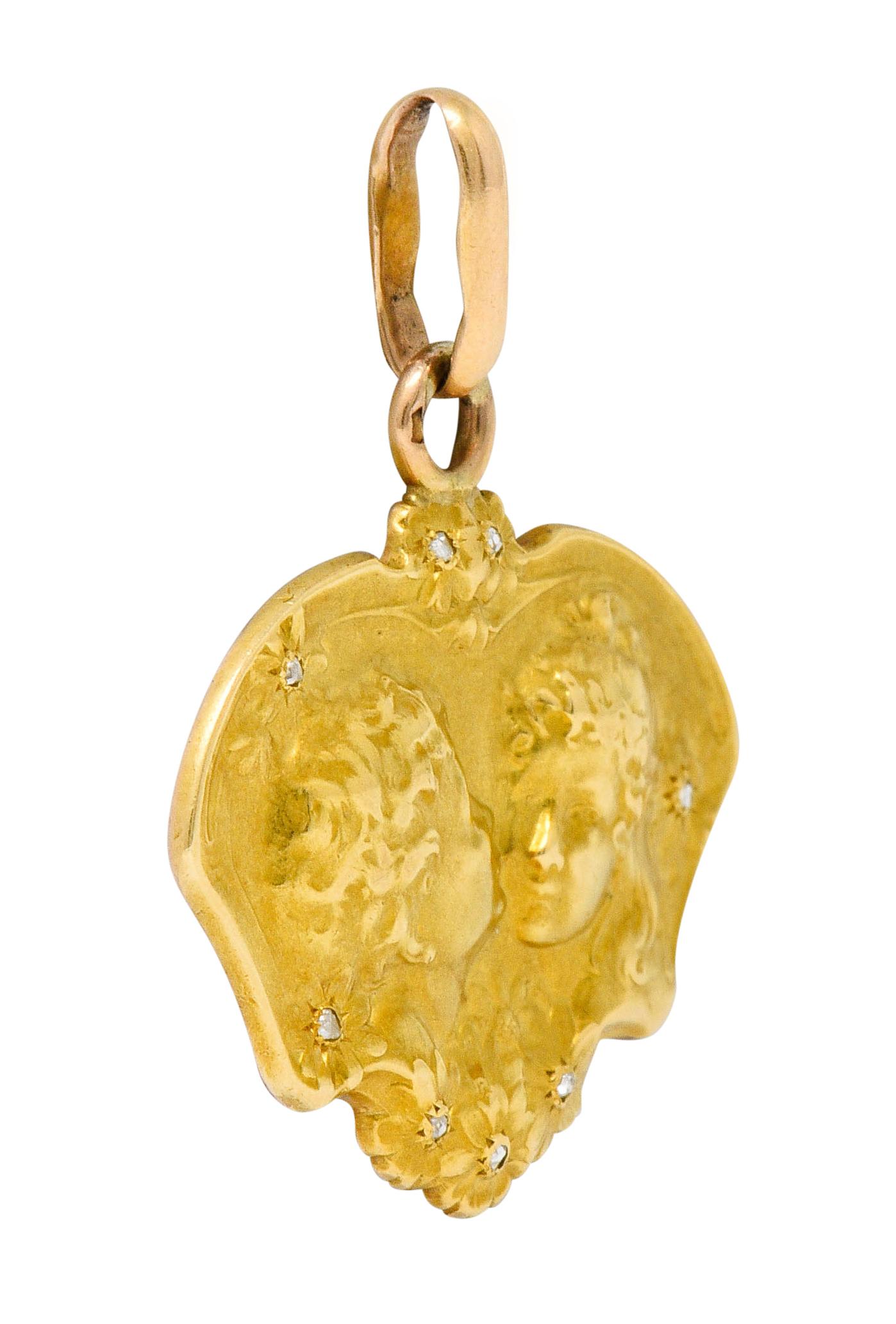 Pendant features highly rendered yellow gold repousse at front

Depicting florals and a little boy kissing a little girl innocently on the cheek

Florals are accented by rose cut diamonds

Back of pendant is rose gold and deeply engraved with a