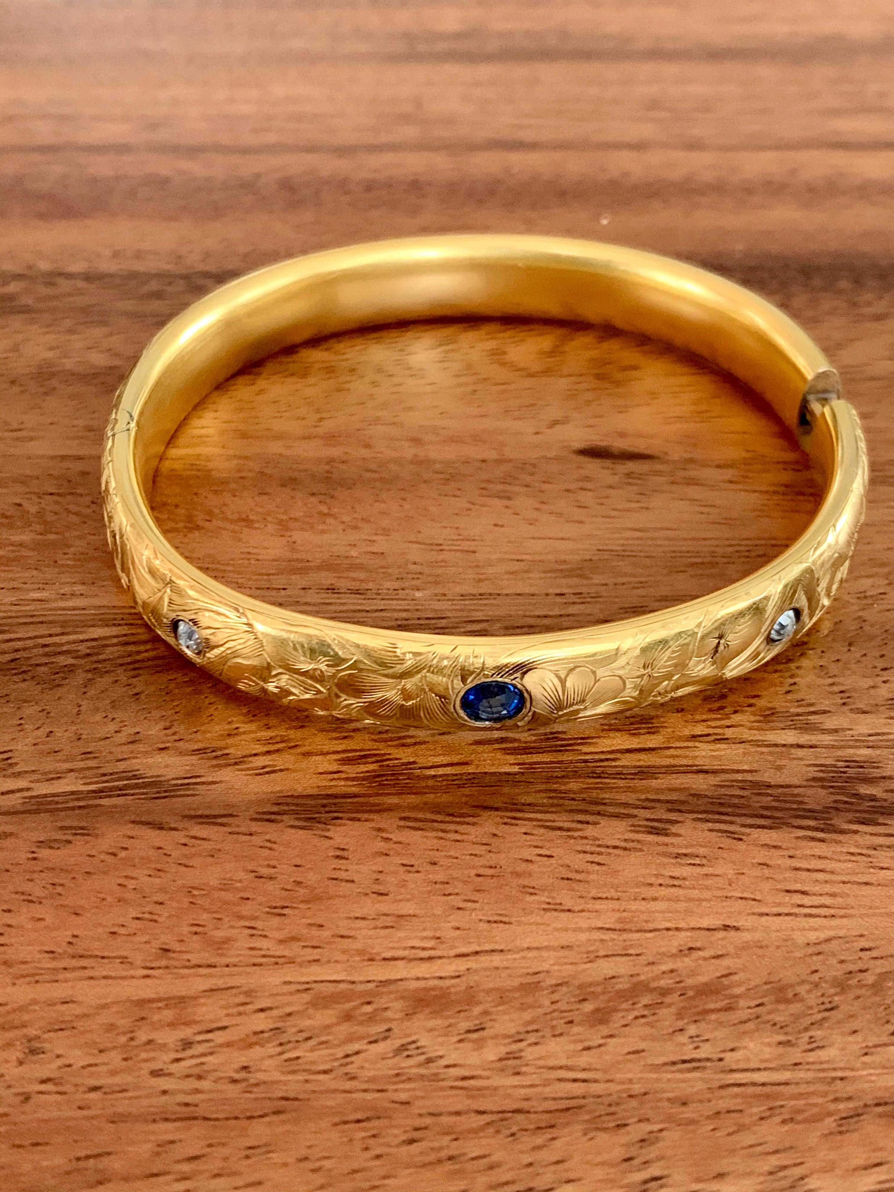This beautiful Art Nouveau hinged bangle bracelet features two 3mm European cut Diamonds at .25ctw and one oval, faceted 7 x 5mm medium blue Sapphire at approximately 1ct. 
Weight: 16.7 
