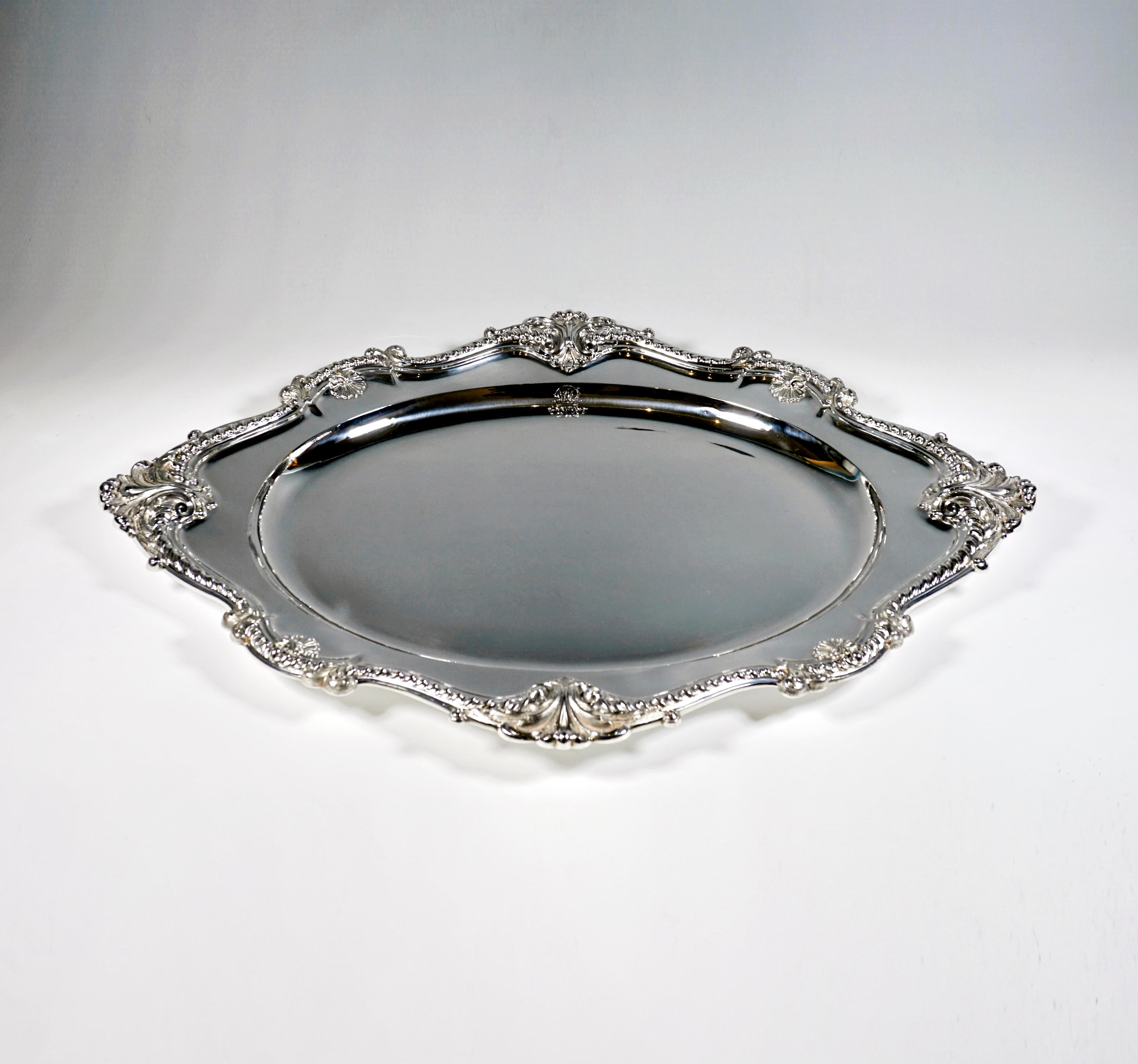 Solid silver tray with an oval mirror, the edge expanding into a diamond shape with surrounding cord, volute and rocaille decorations.

Hallmarks:
Diana's head - Austrian official hallmark 1872-1922 for 900 Silver
'J.C.K' - Manufactory sign of