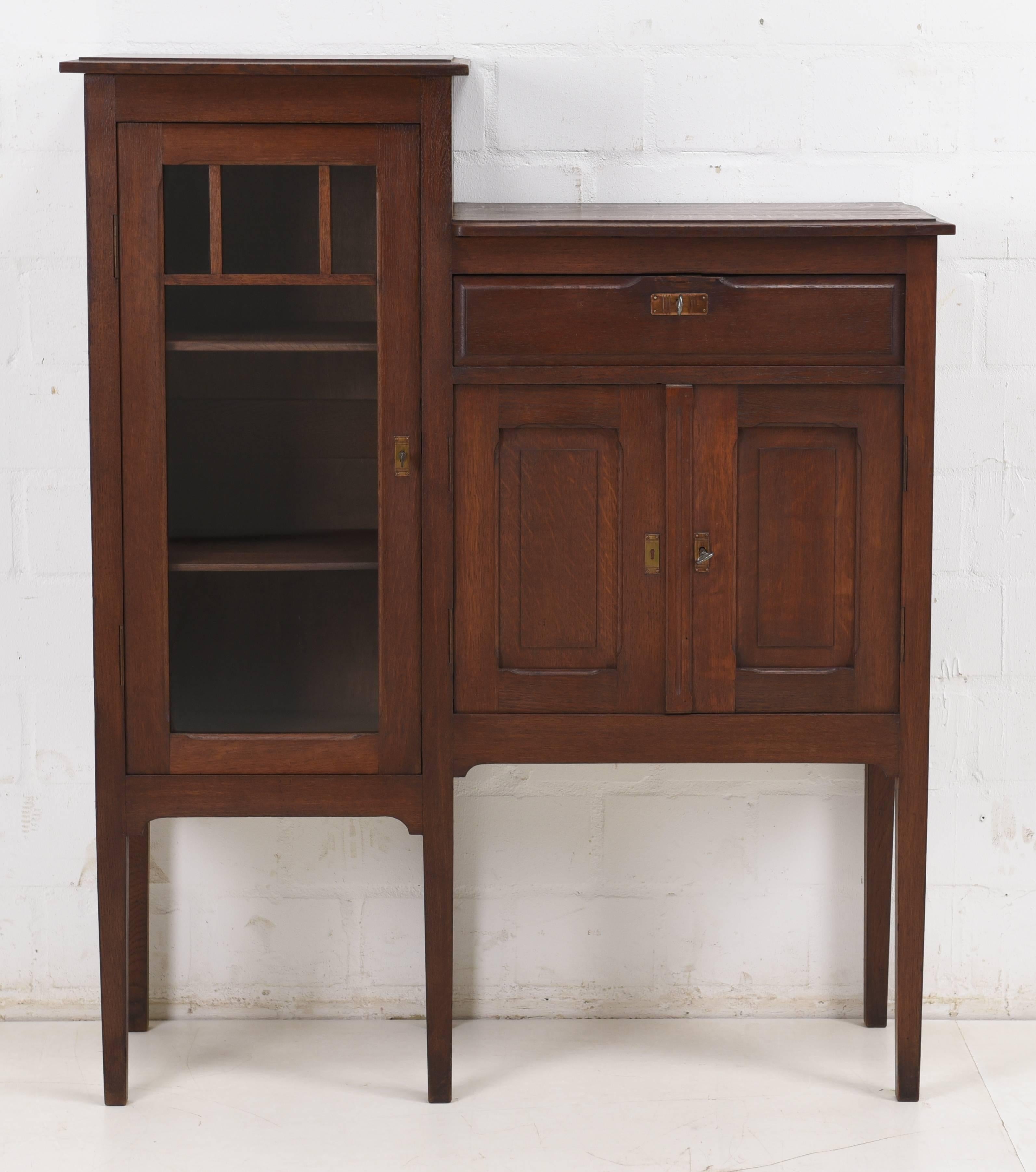 A small asymmetric display cabinet from the Art Nouveau era, circa 1915. The body is made of solid oak and the interior softwood and plywood. Original fittings at the doors with locks and keys. The shelves of the display unit are adjustable in