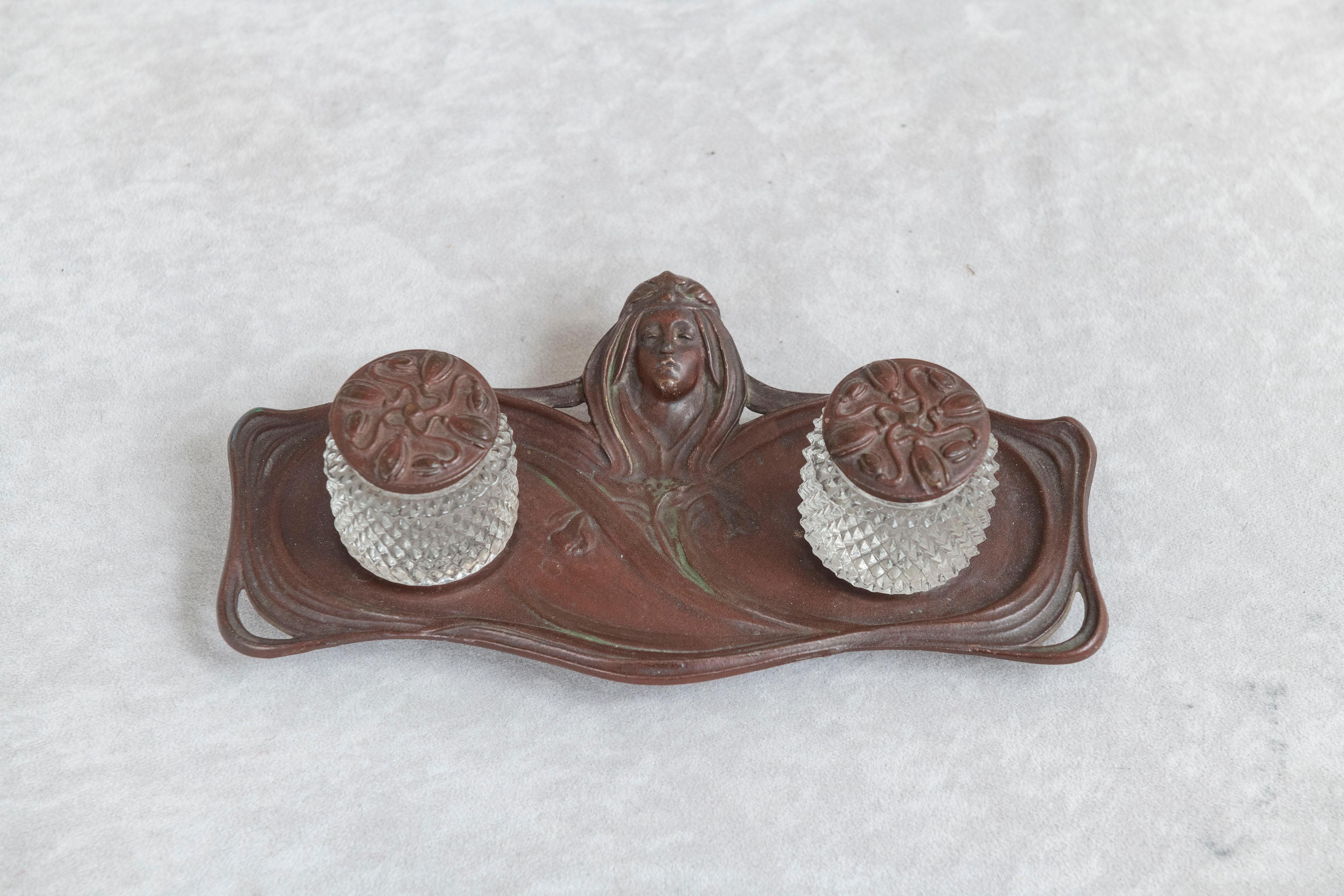 This beautiful little inkwell has a strong commitment to the art nouveau movement. From the cameo of a woman with flowing hair to the finely detailed inkwell lids depicting swirling flowers. We find it amazing that both inkwells are still there with