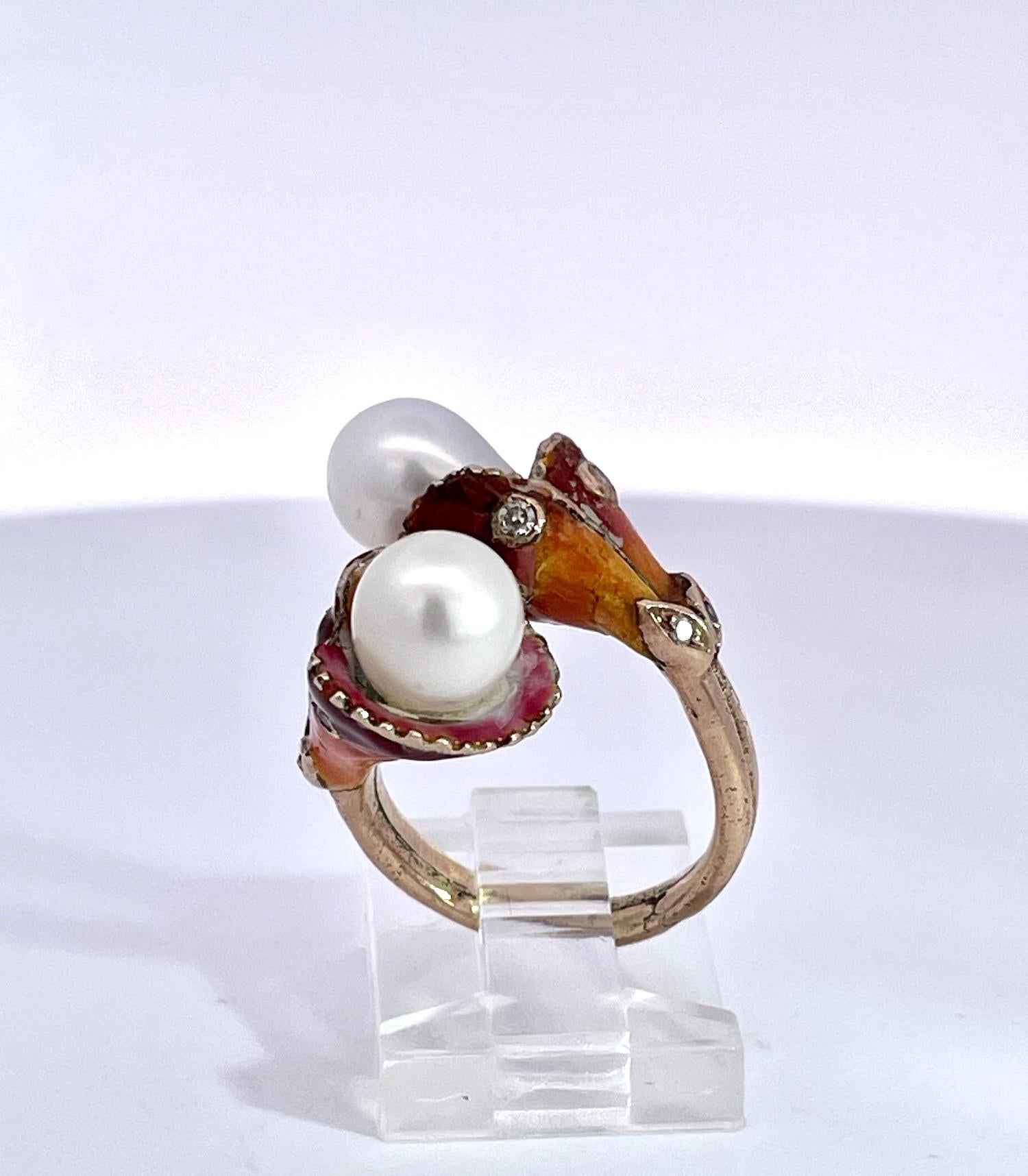Cette bague art nouveau est très particulière car elle comporte deux belles perles dans une monture tulipe en émail.  L'émail est d'un rose profond qui passe à l'orange puis au brun.  L'émail est constellé de diamants.  Deux diamants sur chaque
