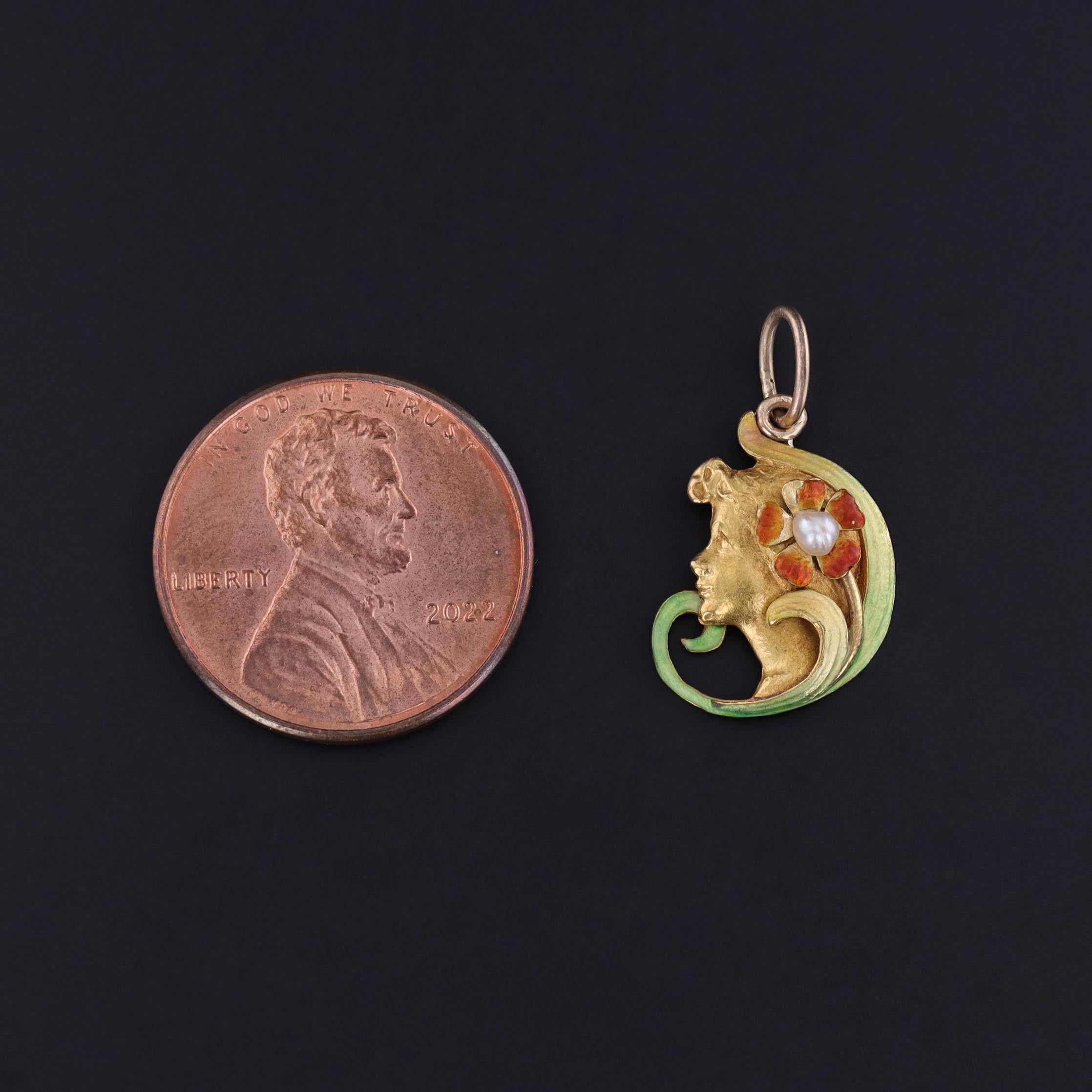 An antique, Art Nouveau era charm featuring a woman of 14k gold with an enamel flower and a pearl, dating to 1900.

The piece measures 0.8 inches from the top of the jump ring to bottom by 0.45 inches wide and weighs 1.53 grams. It is in very good