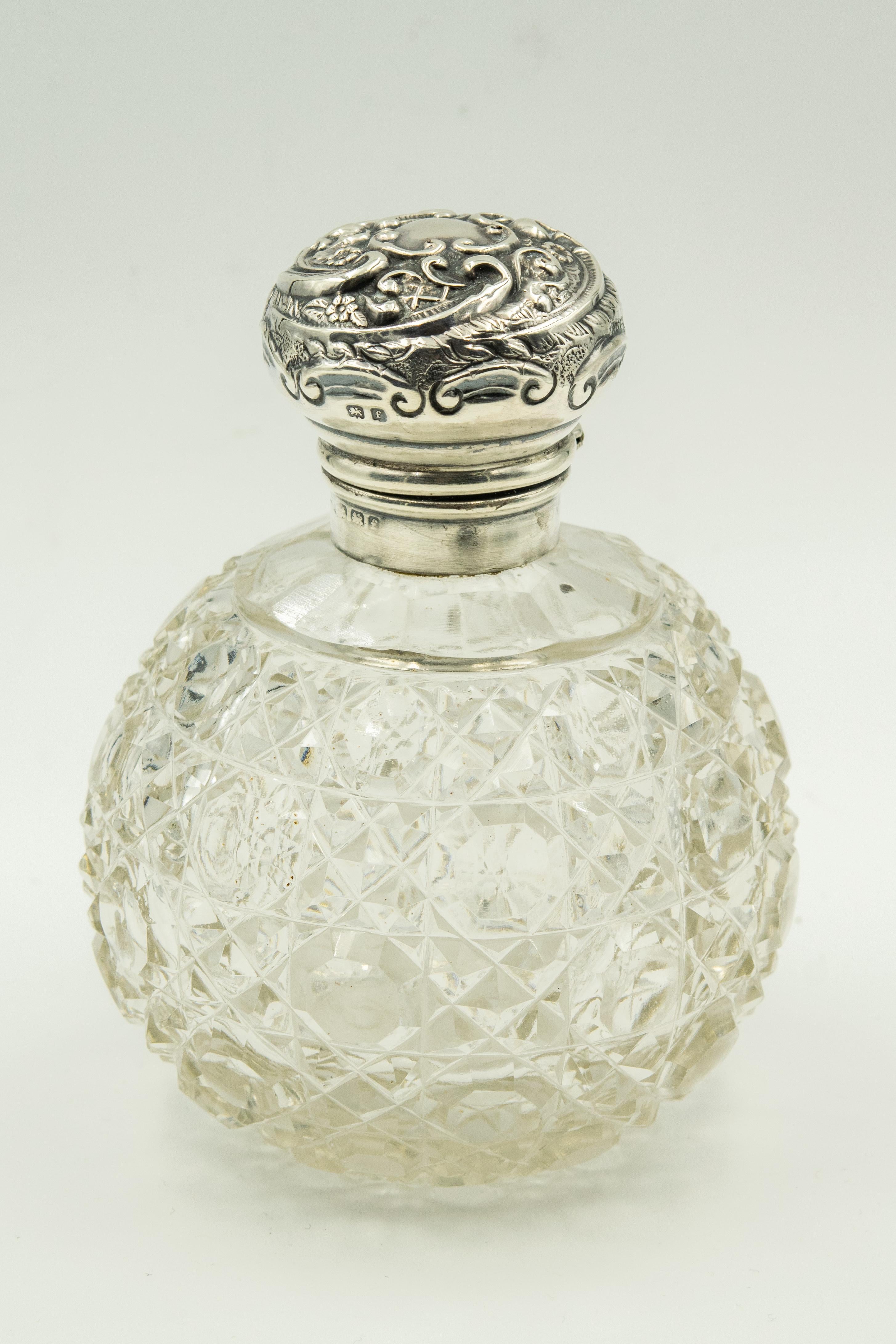 Beautiful English cut crystal perfume bottle with a sterling silver hinged top. The silver mount has a high relief repoussé scroll and flower pattern. The stopper is missing.

Hallmarks for England Birmingham and date letter F for 1905. The makers