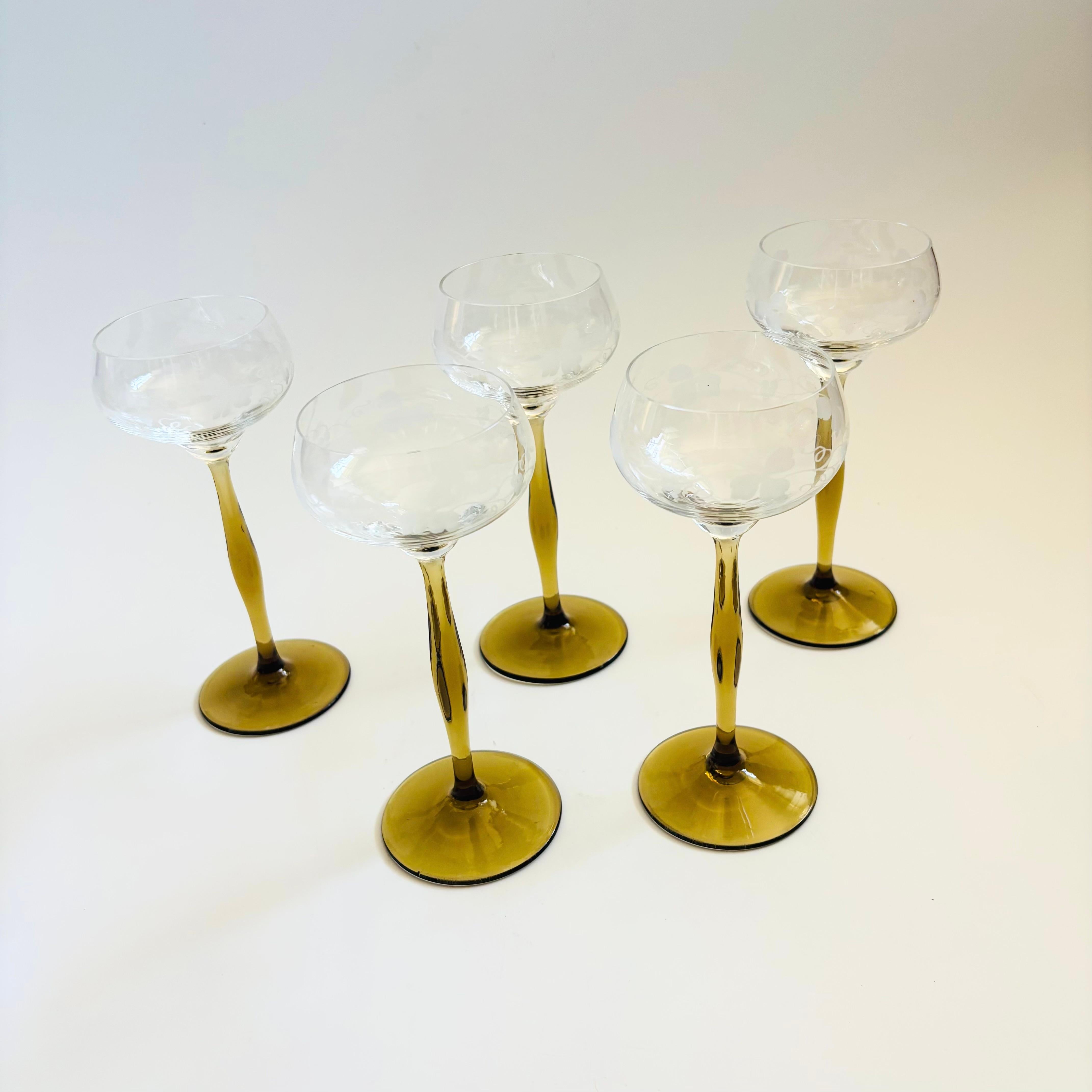Juego de 5 copas de champán art nouveau de estilo Peter Behrens. Cada una tiene un tallo de color oliva apagado que varía de grosor. Cuencos de cristal transparente con un diseño grabado de hojas de parra.

