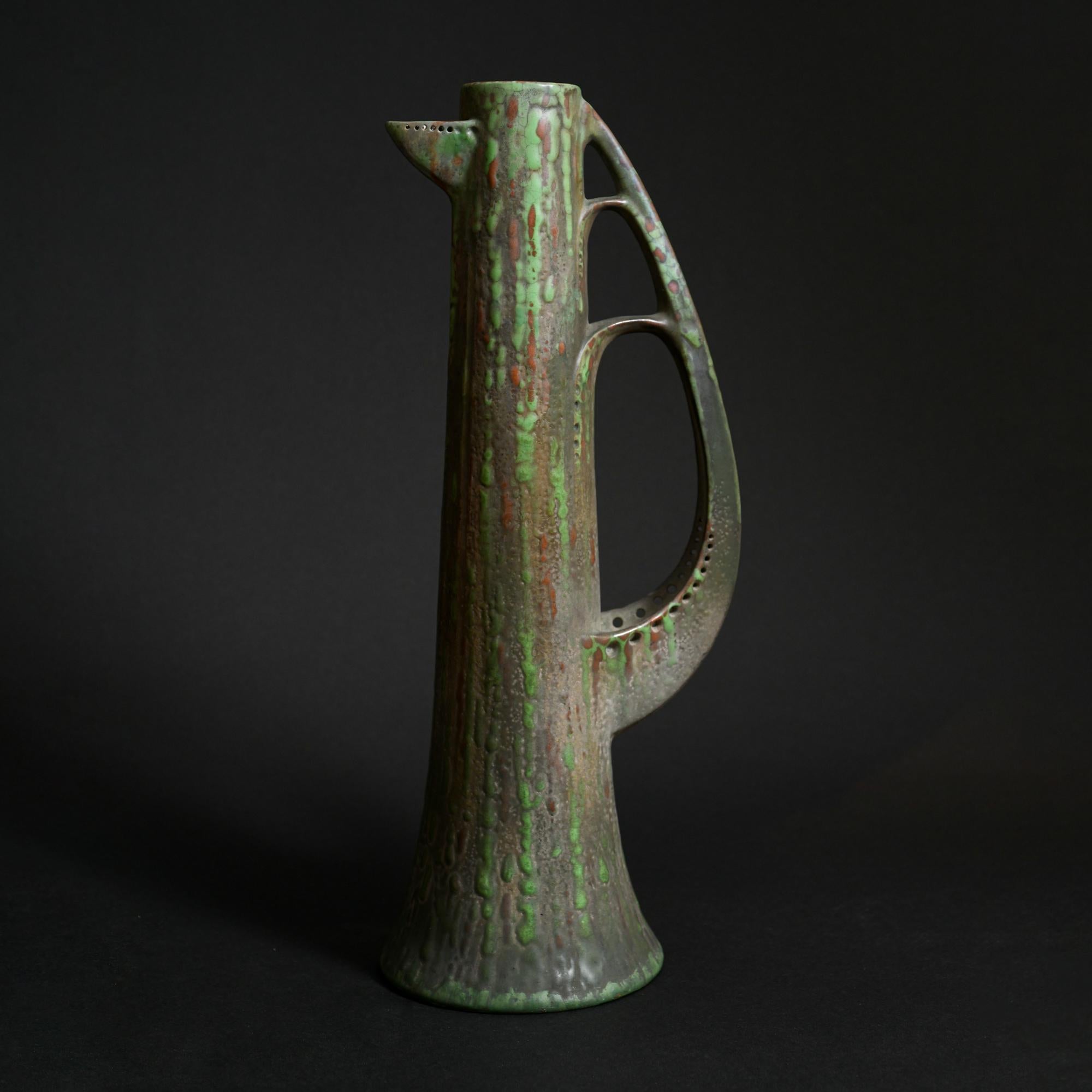 Austrian ceramist Paul Dachsel designed this unusually shaped pitcher, made of hard earthenware and covered in a light green glaze. Its slim and elongated body gives the piece an elegant look, accentuated by a highly stylized handle that evokes