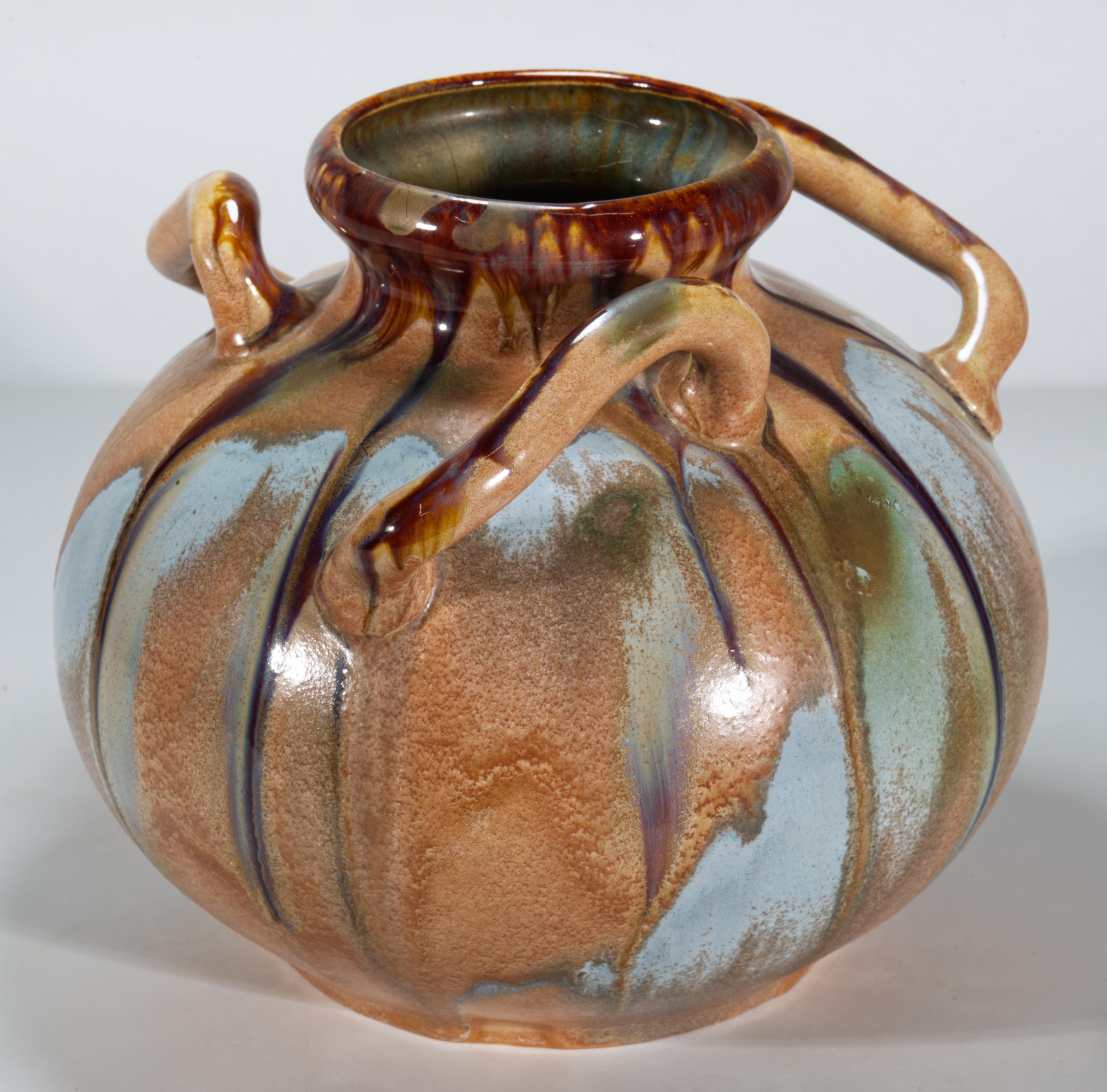 Striking large ceramic vase features the organic, rounded shape with 3 curved, free-flowing decorative handles. It is decorated in characteristic Belgian Art Nouveau style with the use of warm, earthy tones and varied glaze finish, creating light