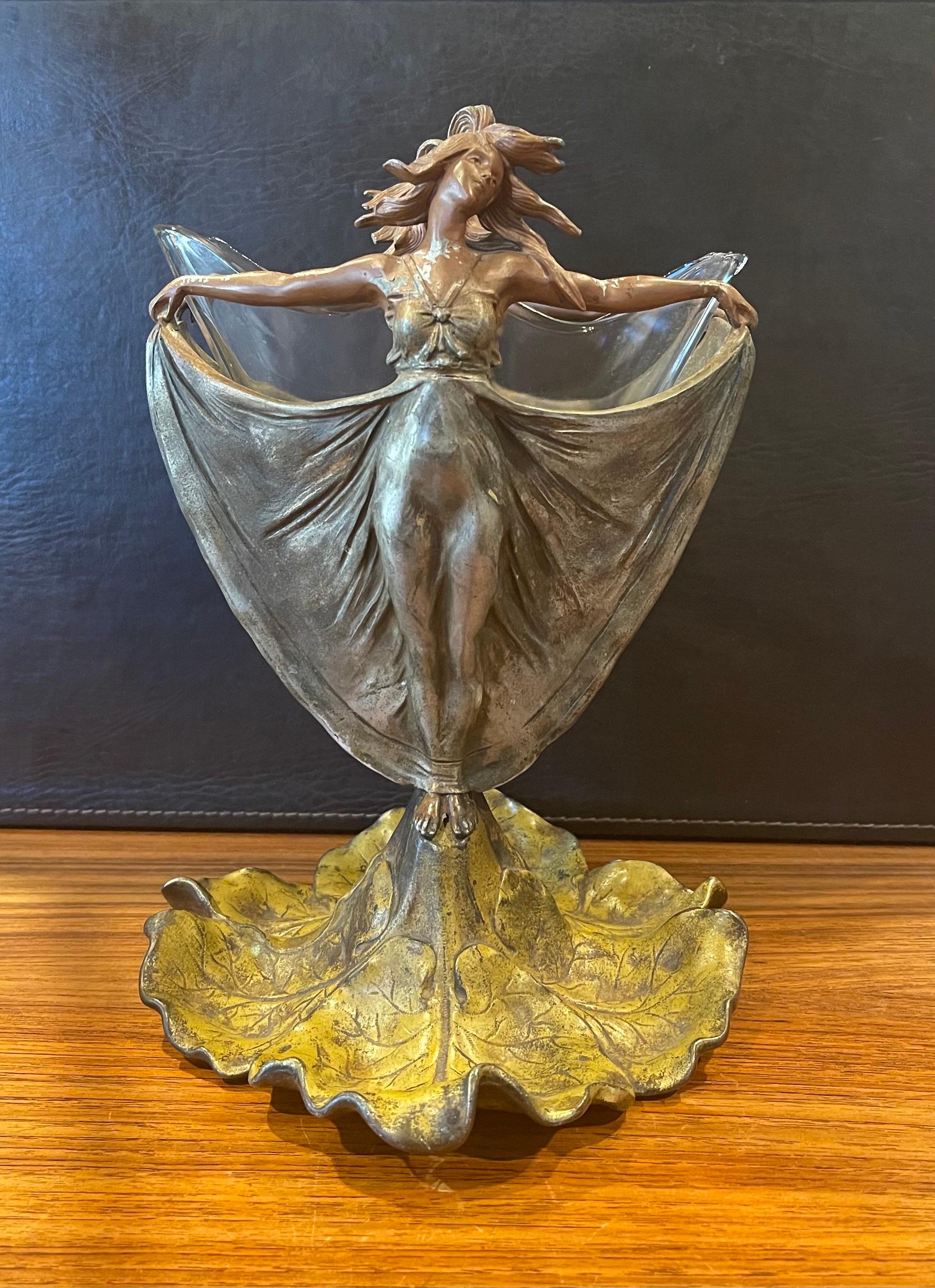 Wonderful Art Nouveau cast metal figural vase with glass insert, circa 1910s. The form of the design features a pair of women in flowing gowns with outstretched arms holding the hem of their dress standing on a lily pad; the piece is unmarked. The